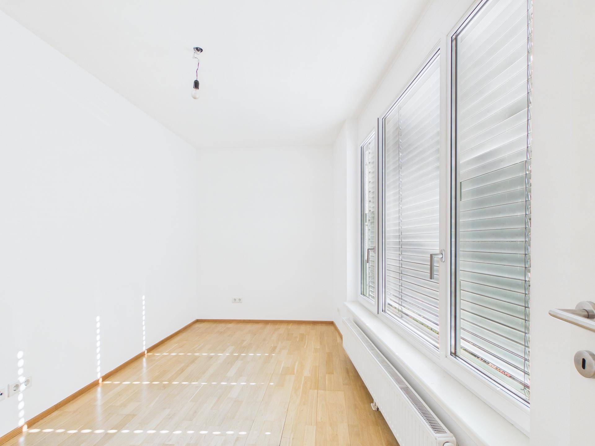 Helles Schlafzimmer mit Holzboden und großen Fenstern mit Jalousien.