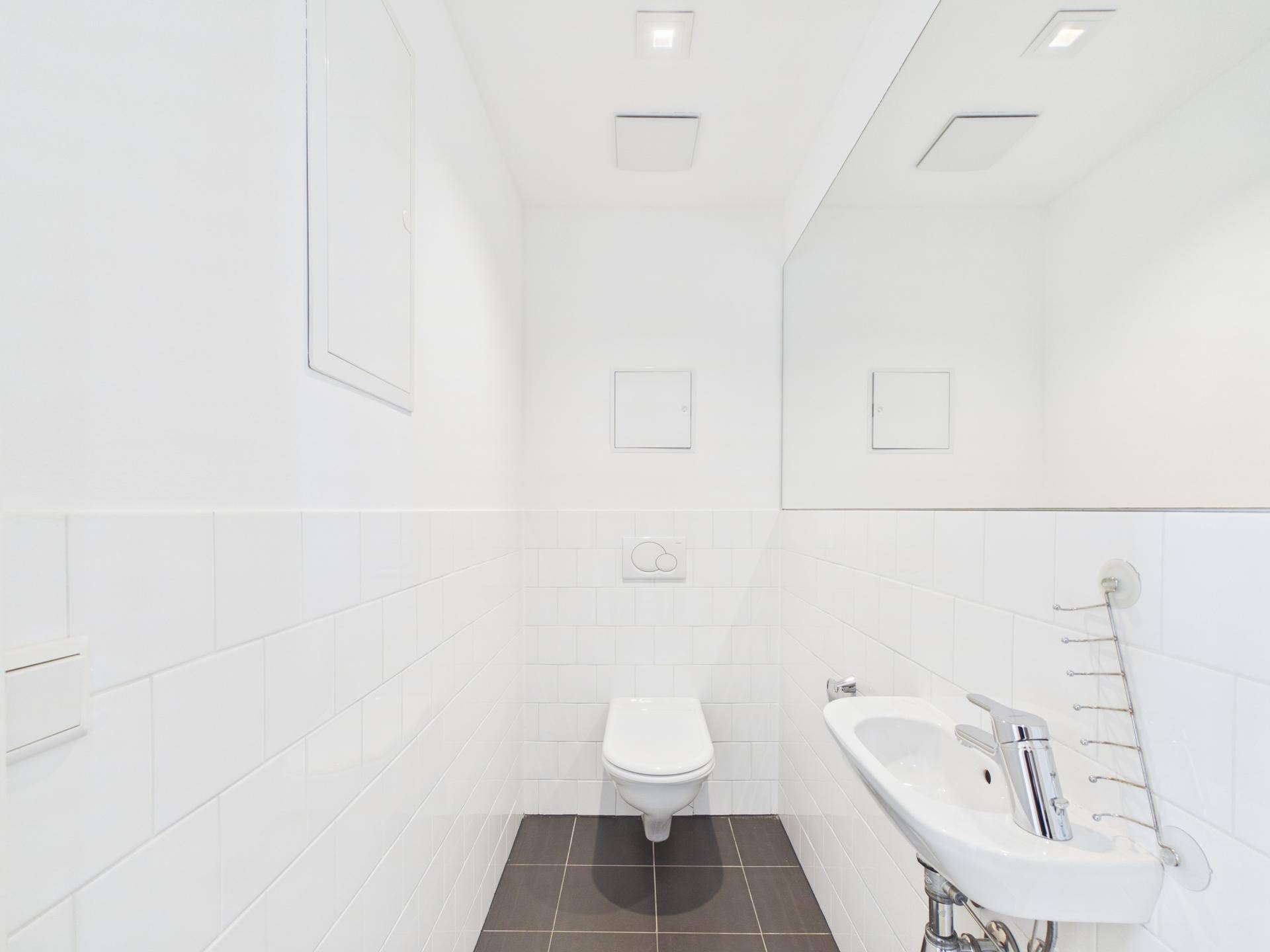 Modernes Gäste-WC mit weißen Fliesen, dunklem Boden und Wand-WC.
