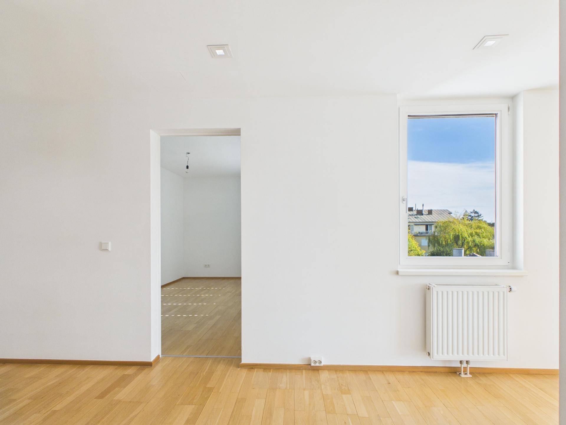 Leerer Raum mit hellem Holzboden und Fenster, bereit zur individuellen Gestaltung.