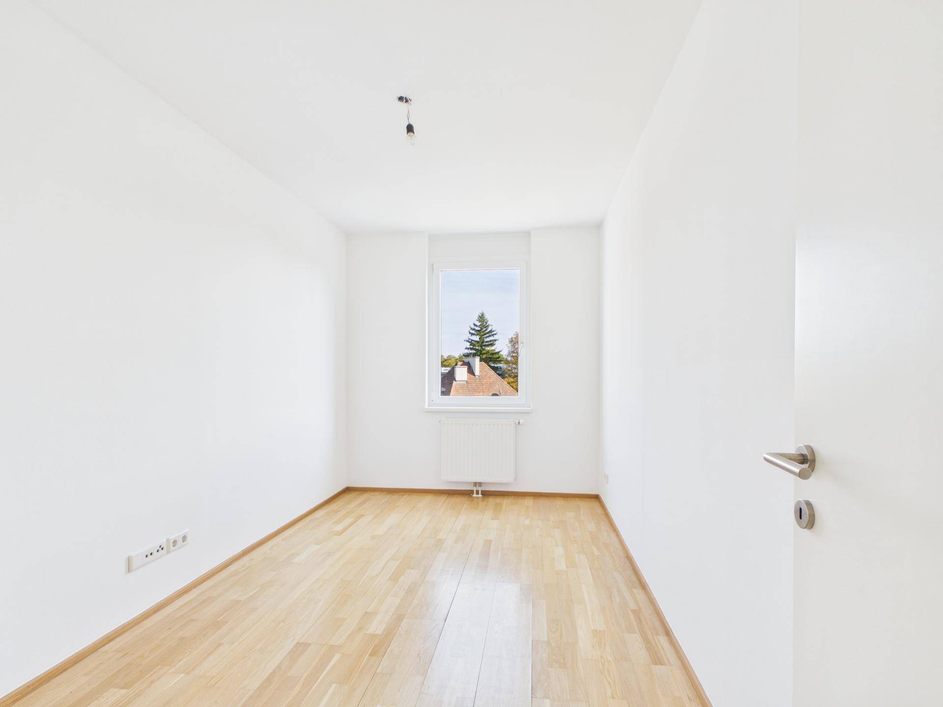 Leeres Zimmer mit Holzboden und Fenster, ideal als Schlaf- oder Arbeitszimmer.