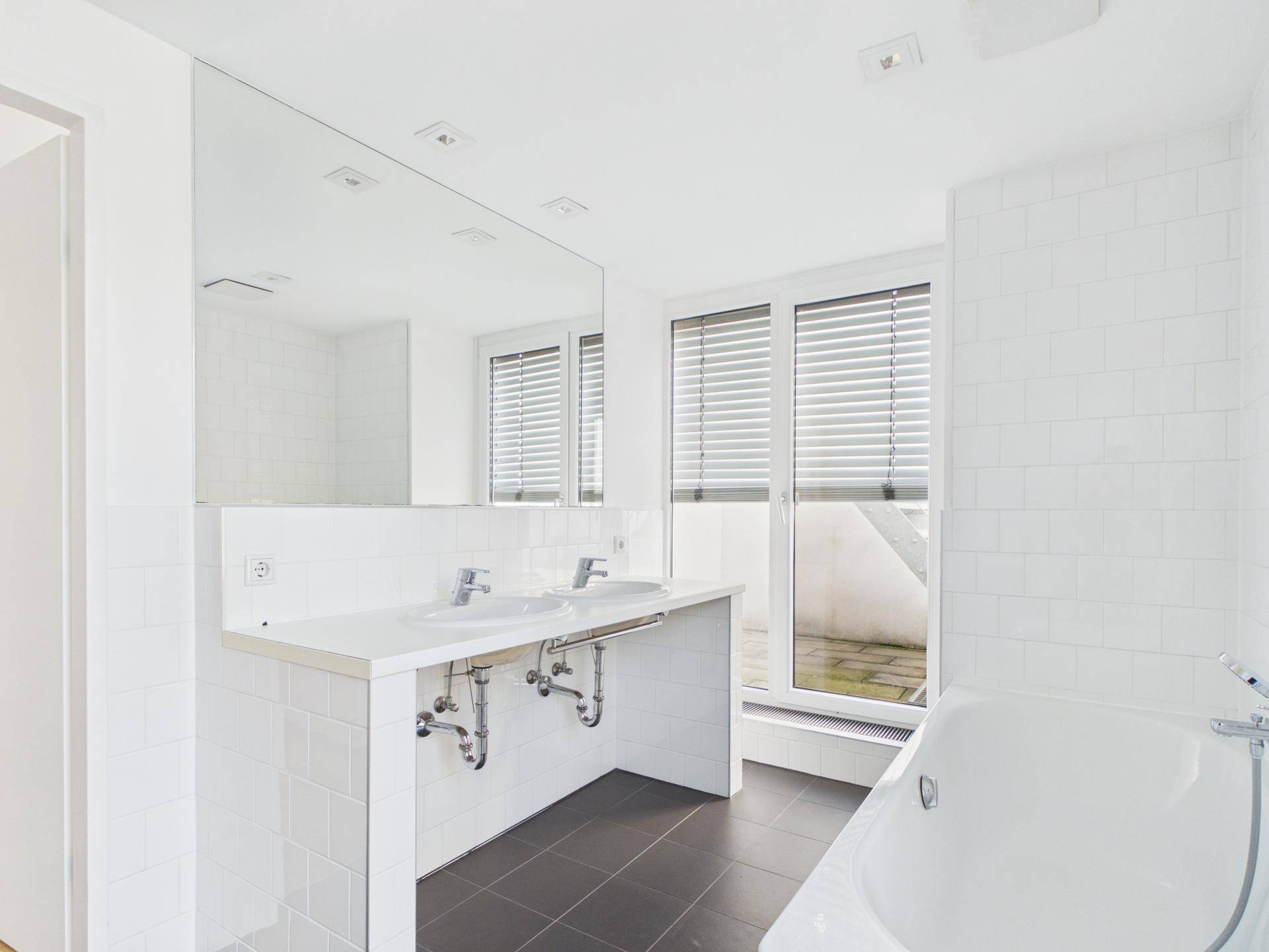 Modernes Badezimmer mit Doppelwaschbecken, Badewanne und Zugang zur Terrasse.