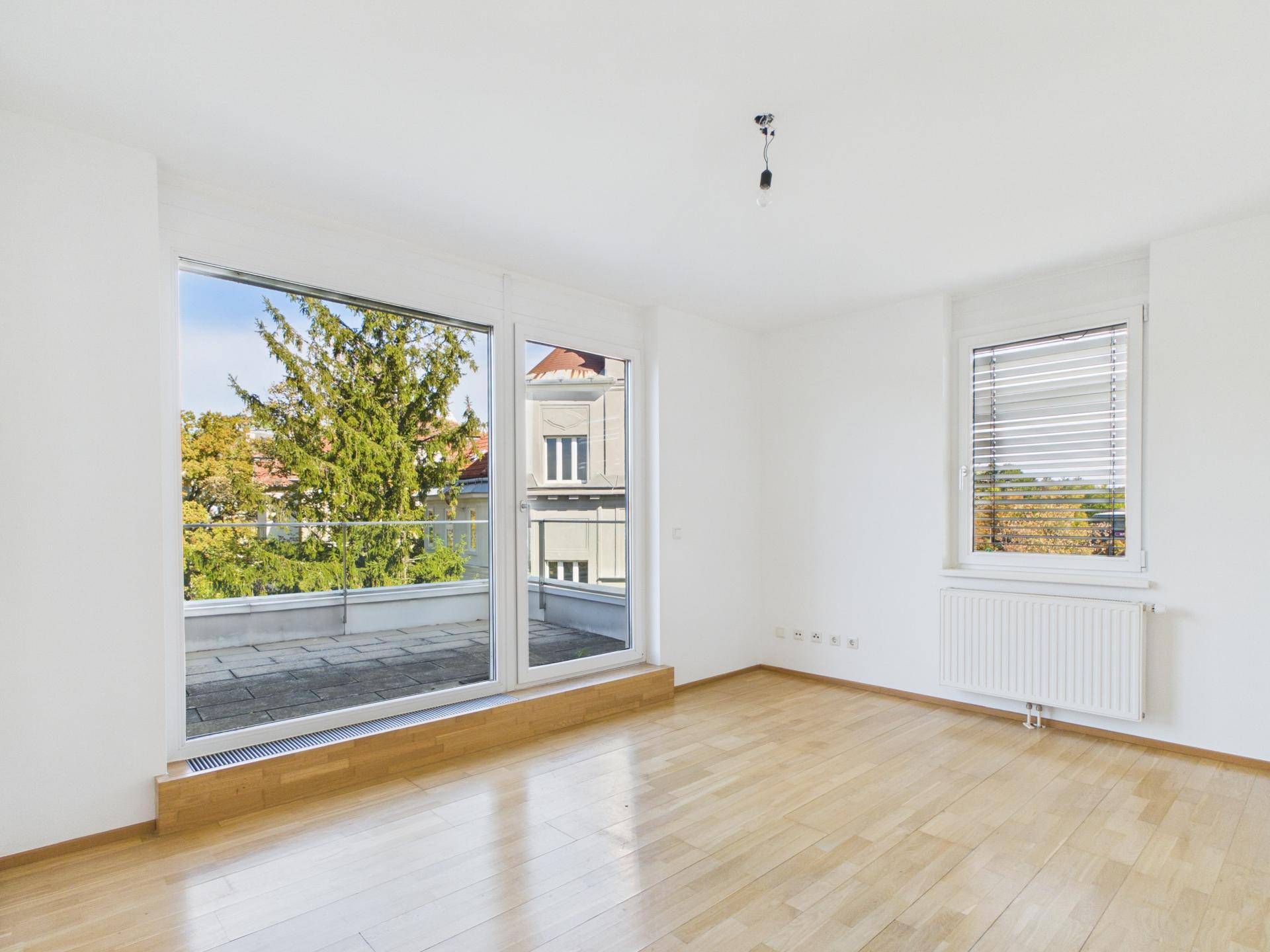 Geräumiges Wohnzimmer mit Holzboden und großen Fenstern mit Blick ins Grüne.