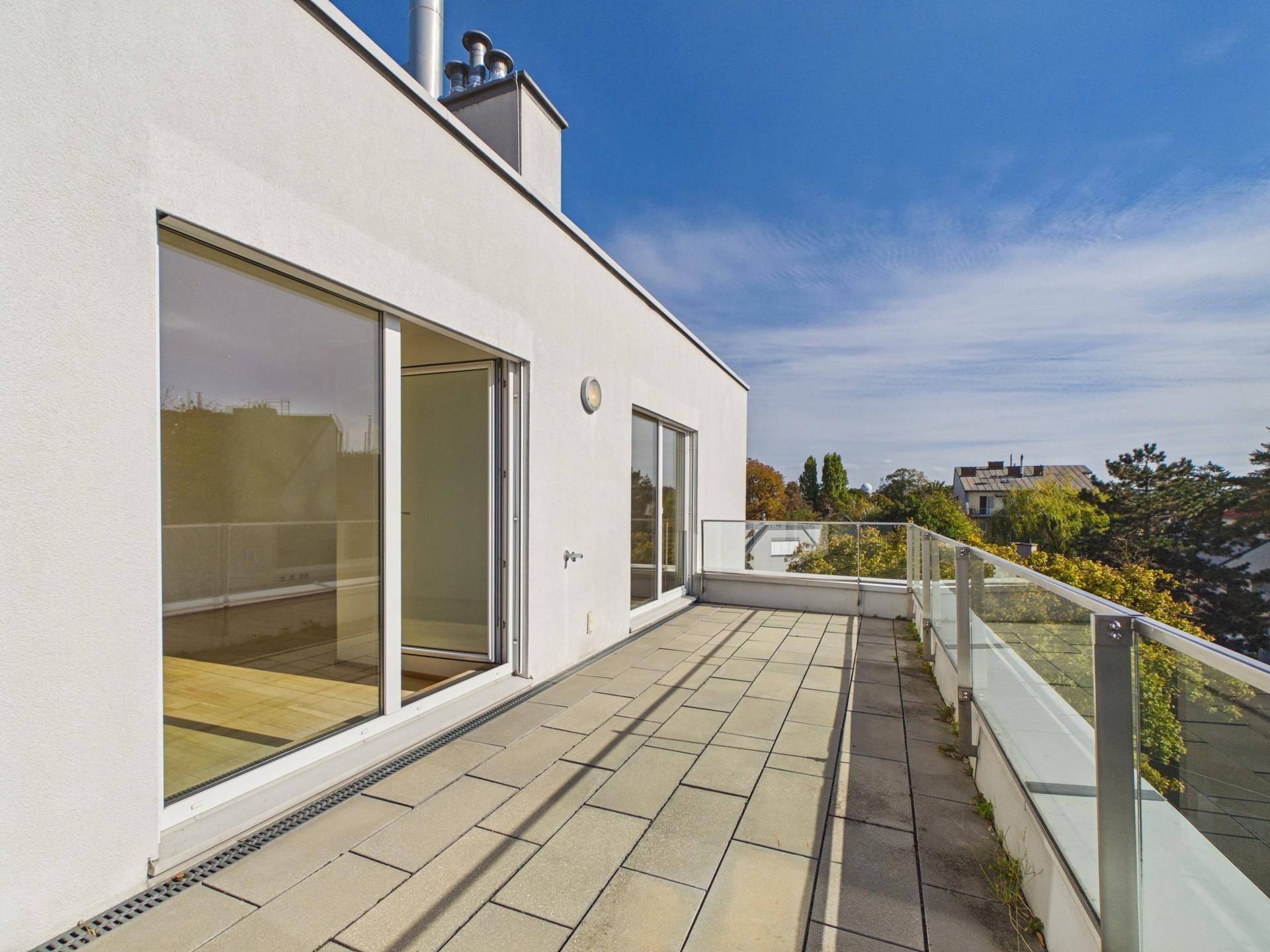 Große Terrasse mit Glasgeländer und Blick auf die grüne Umgebung.