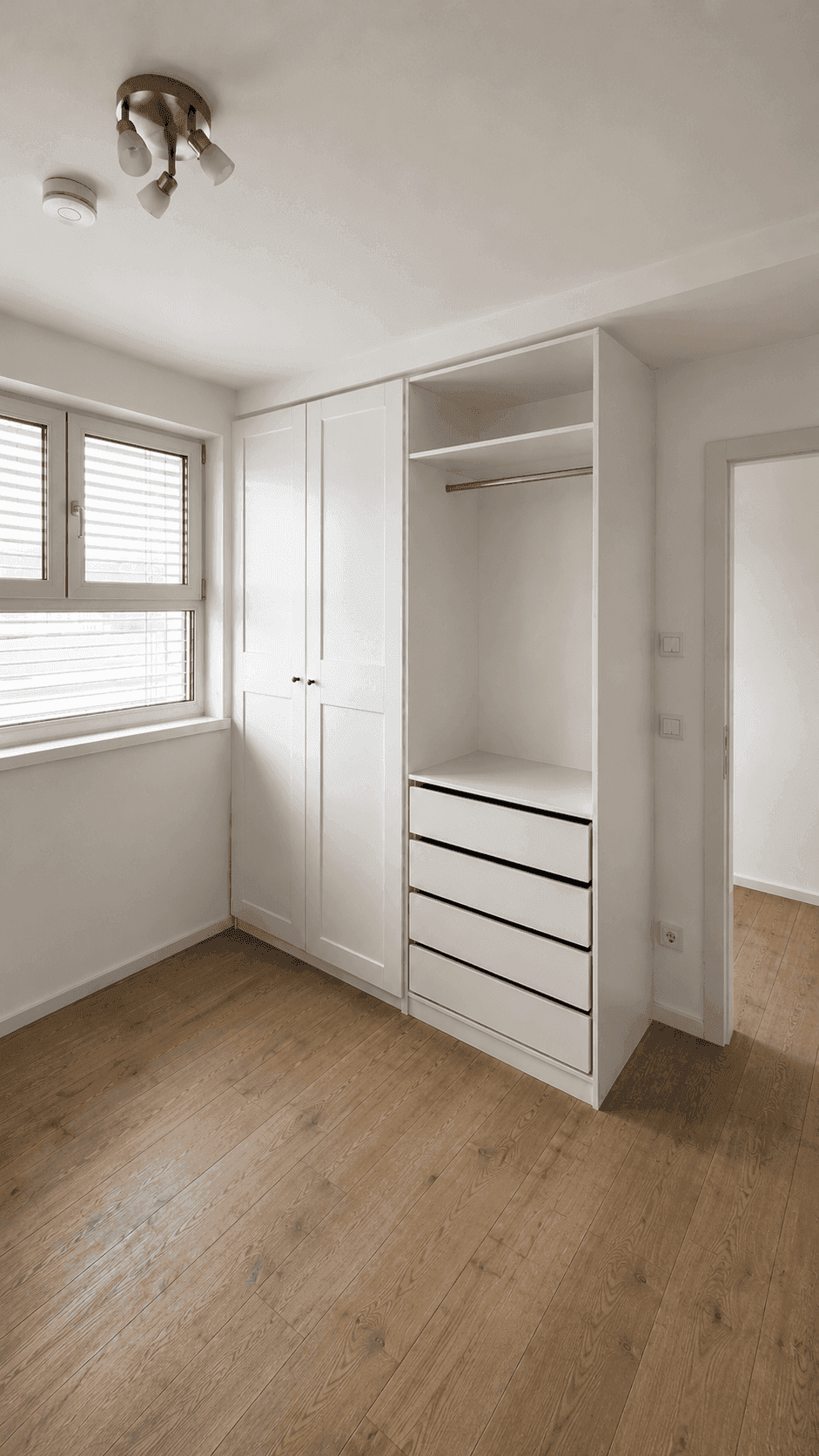 Schlafzimmer mit Holzboden, Fenster und einem praktischen Einbauschrank mit offenen Fächern.