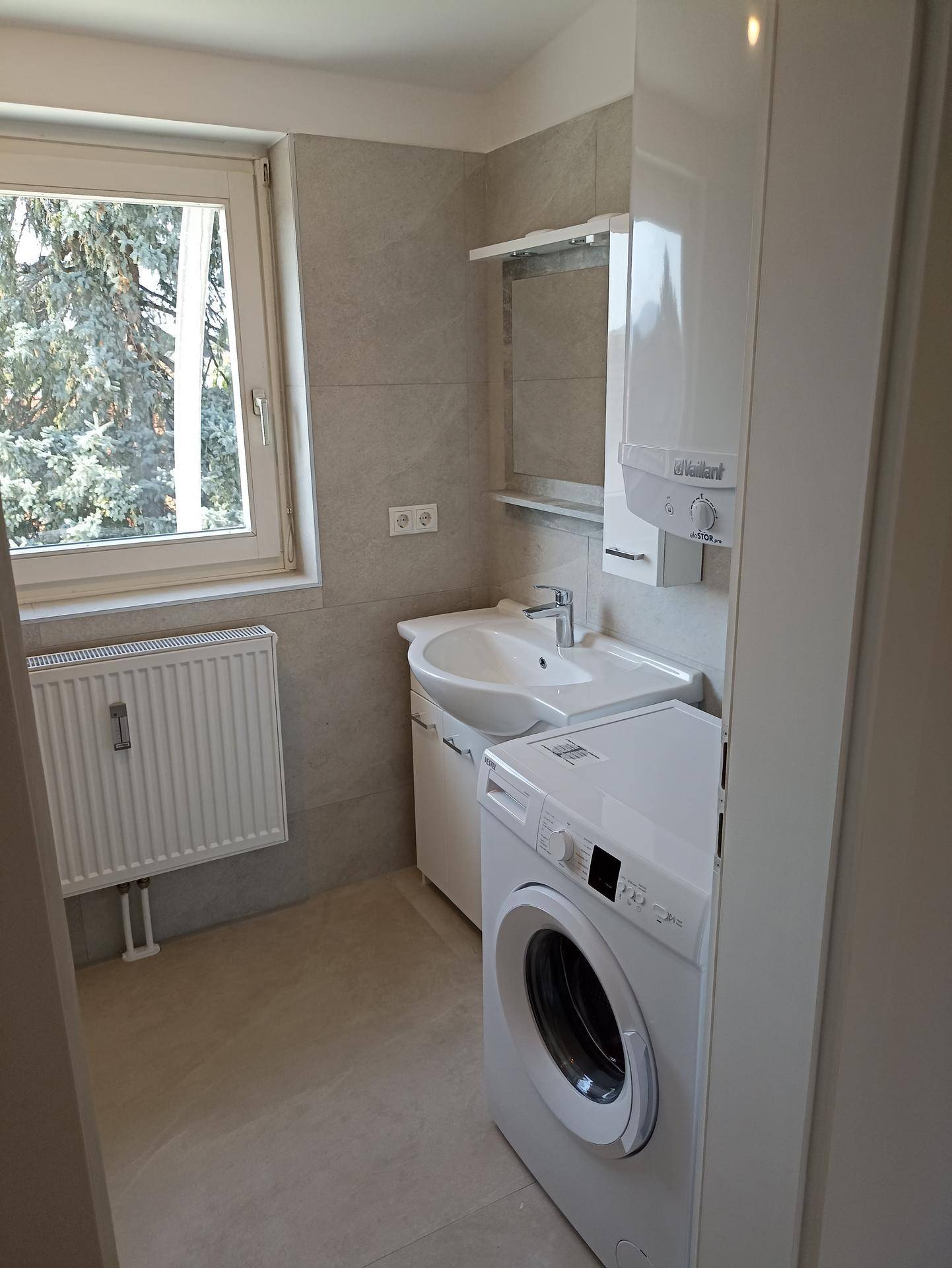 Funktionales Badezimmer mit Waschbecken, Spiegelschrank, Waschmaschine und Fenster für Tageslicht.