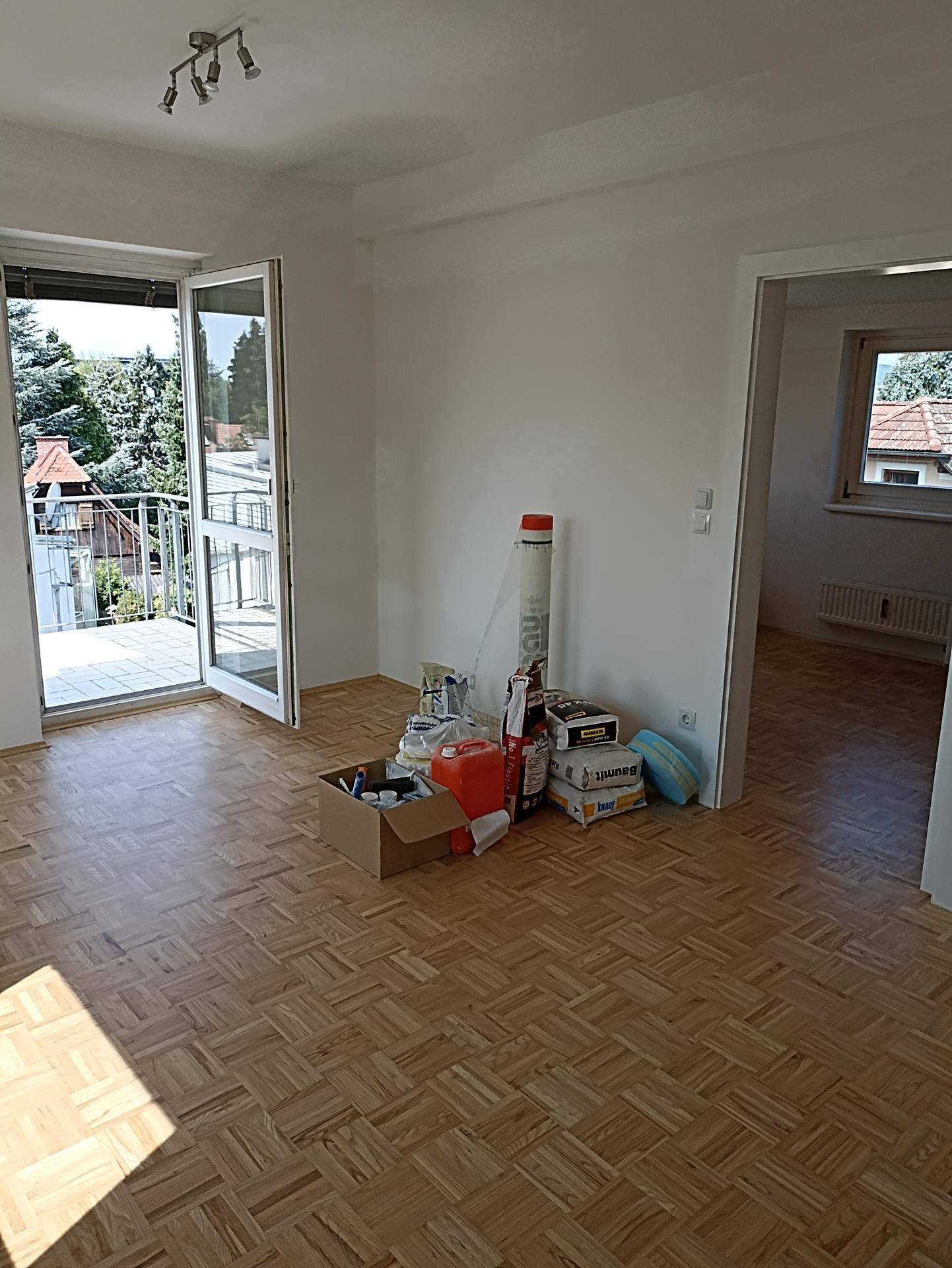 Helles Wohnzimmer mit Parkettboden und Zugang zu einem Balkon mit Blick ins Grüne.