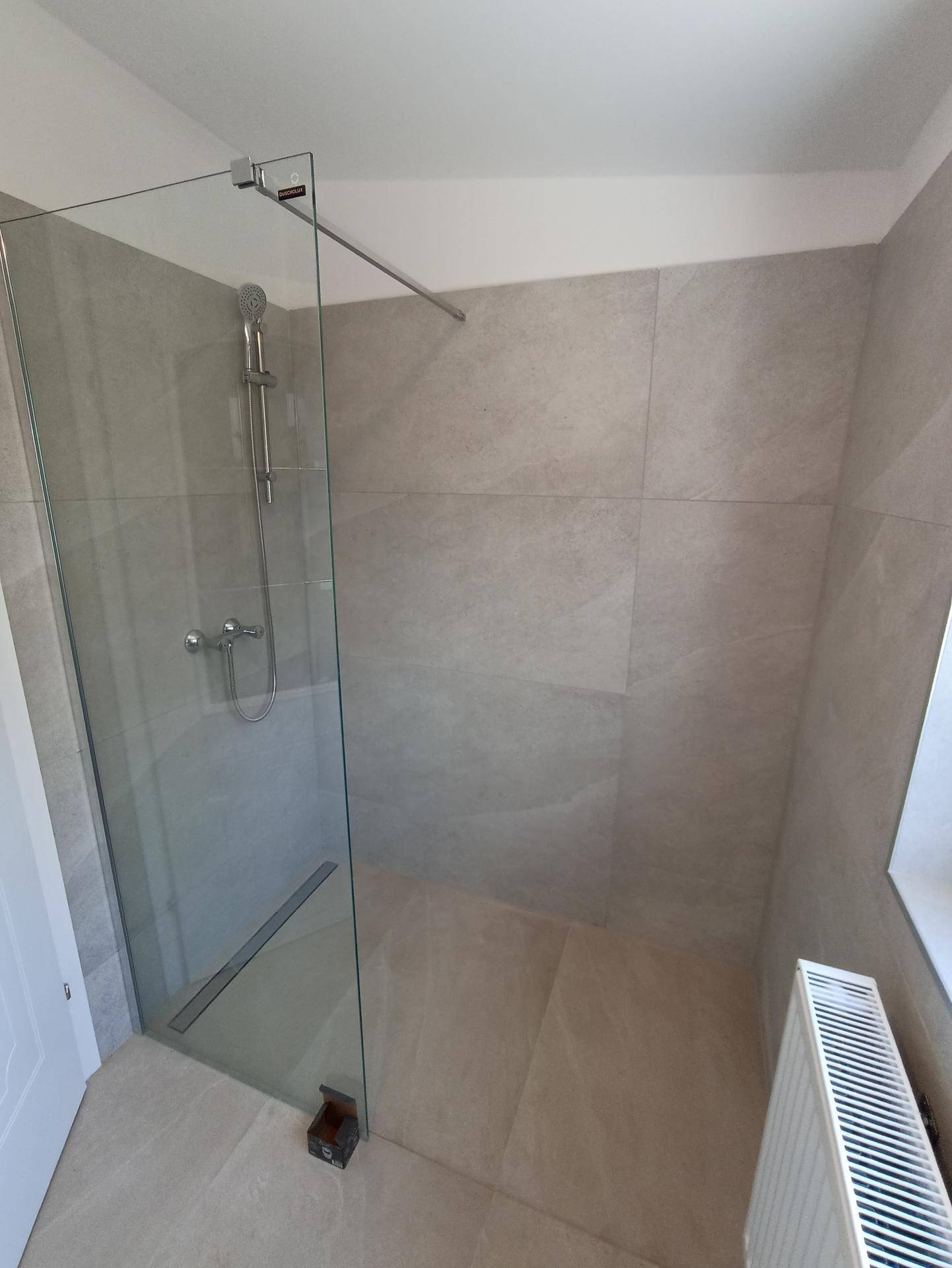 Geräumige Dusche mit Glaswand und hellen Fliesen, inklusive Heizkörper und kleinem Fenster.