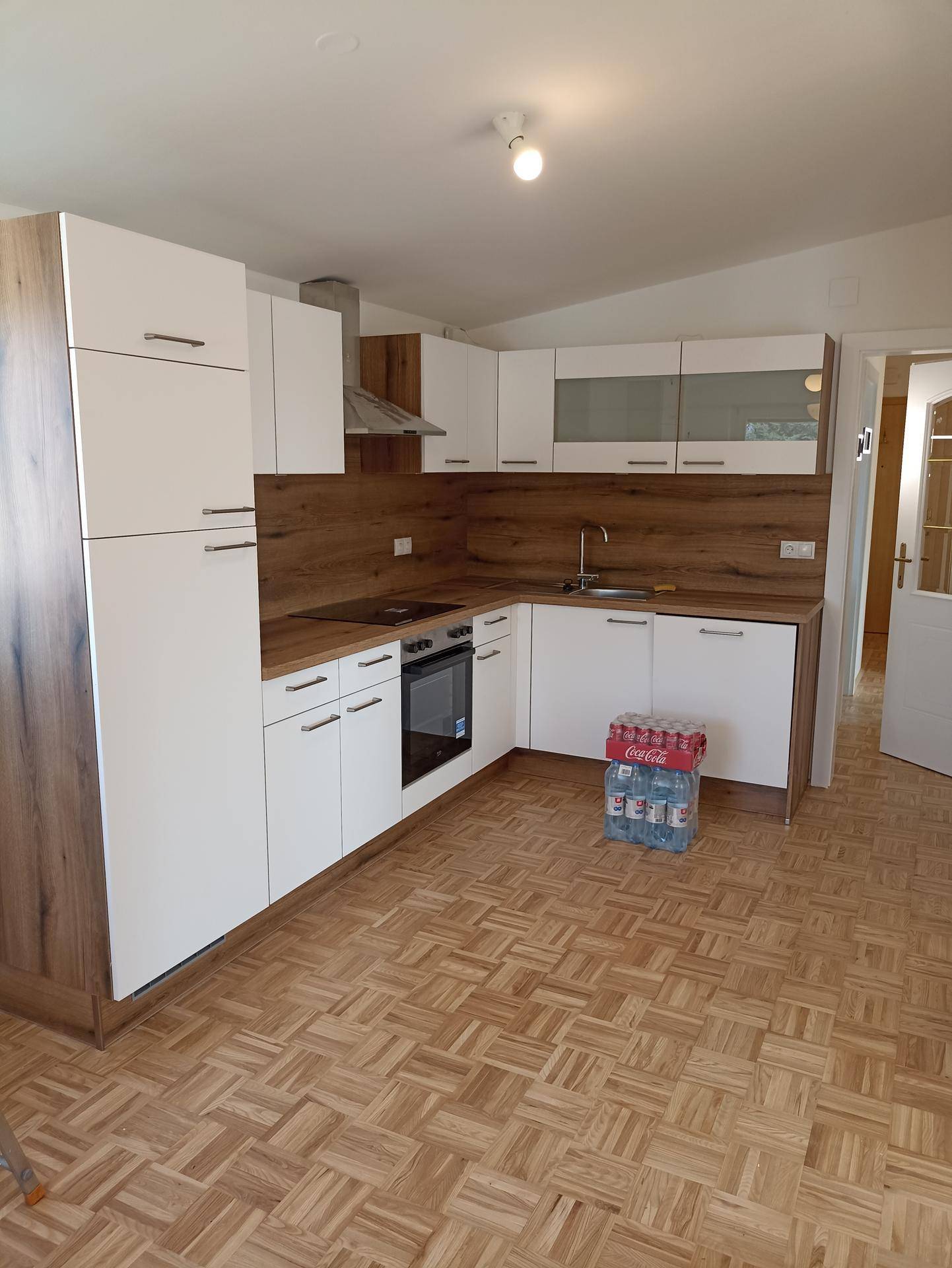 Neue Einbauküche mit weißen und holzfarbenen Fronten, ausgestattet mit modernen Geräten und Parkettboden.