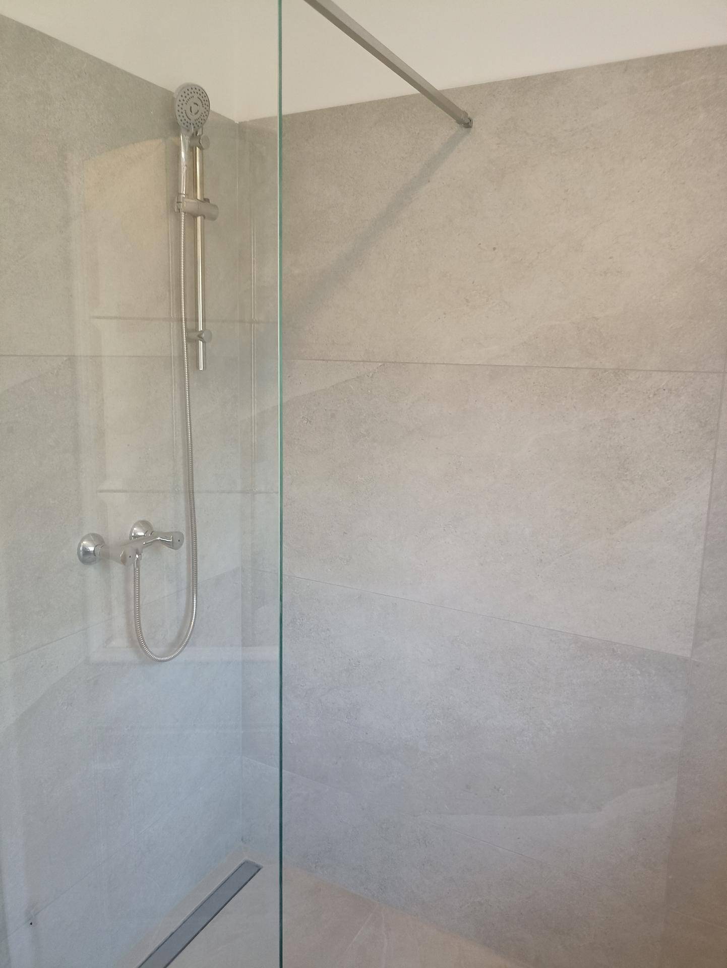 Moderne Duschkabine mit hellgrauen Fliesen und Glasabtrennung in einem Badezimmer.