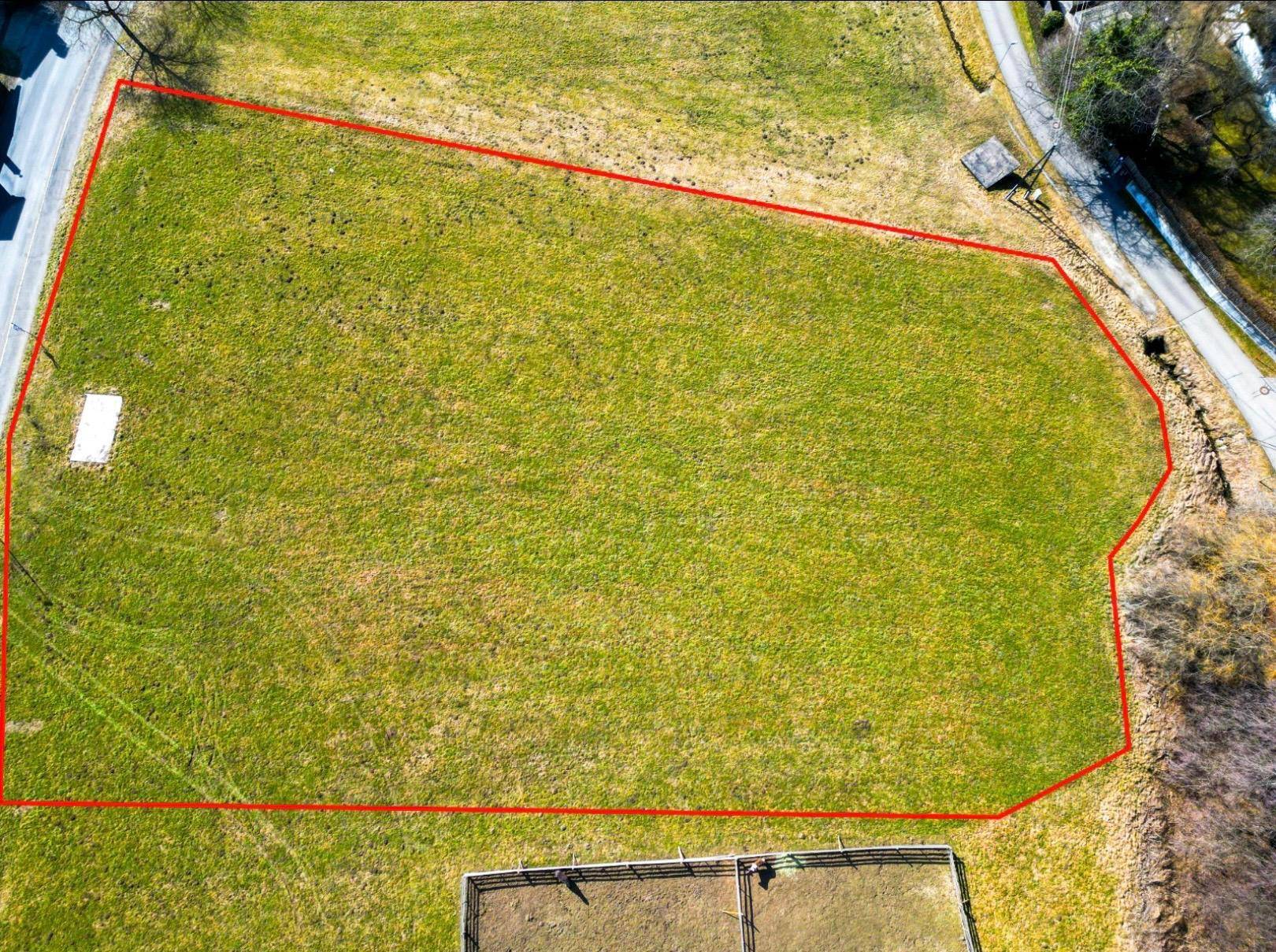 Grundstücksgrenzen markieren das weitläufige grüne Areal mit angrenzender Straße und Zaun.