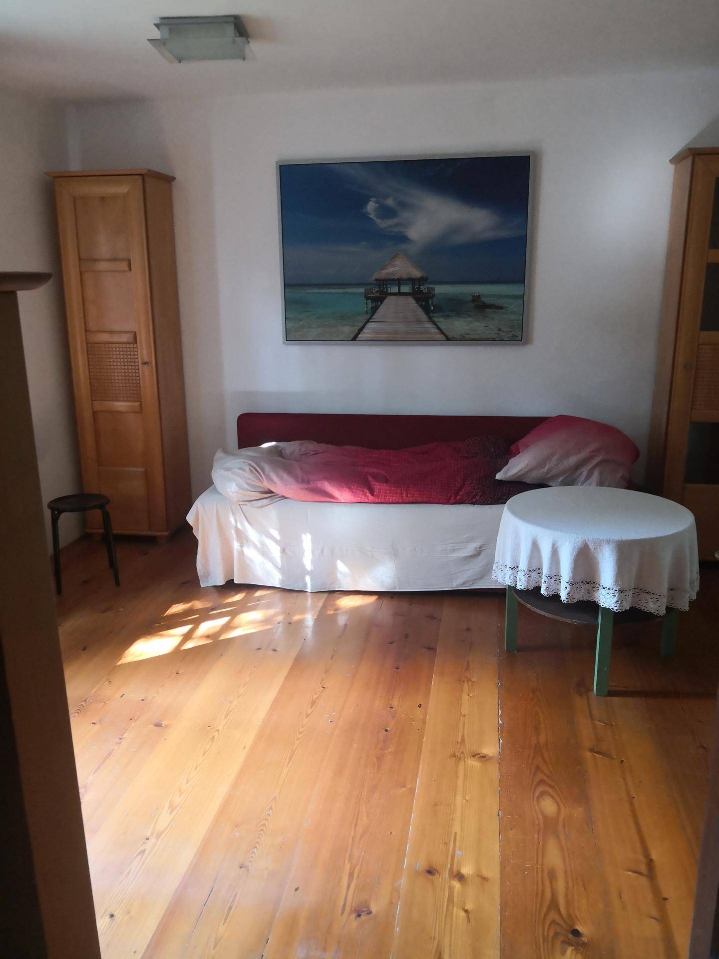 Helles Schlafzimmer mit Holzboden, Bett, Holzschränken und einem Bild an der Wand.