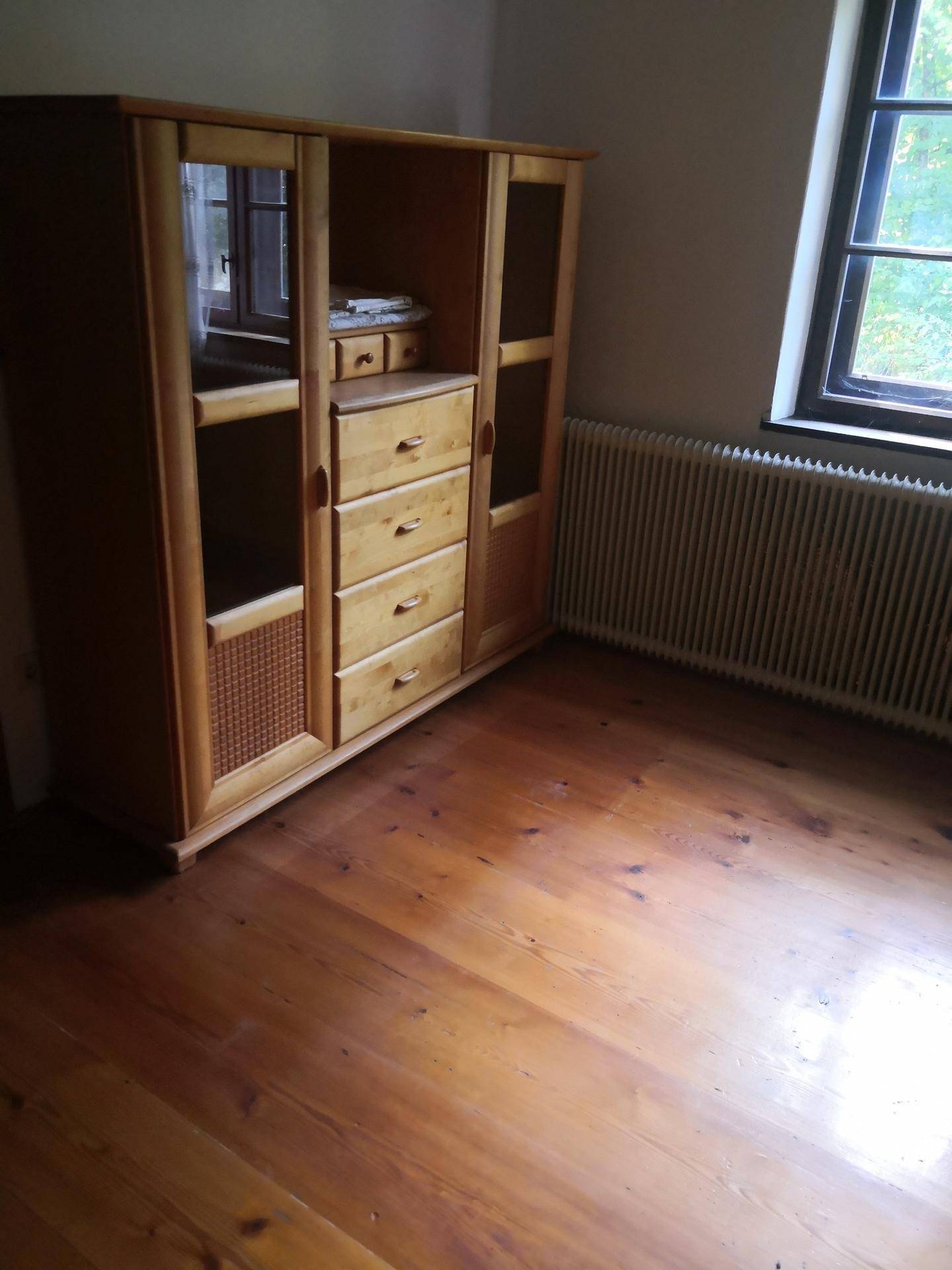 Großer Holzschrank mit Spiegeln und Schubladen neben einem Fenster und Heizkörper.