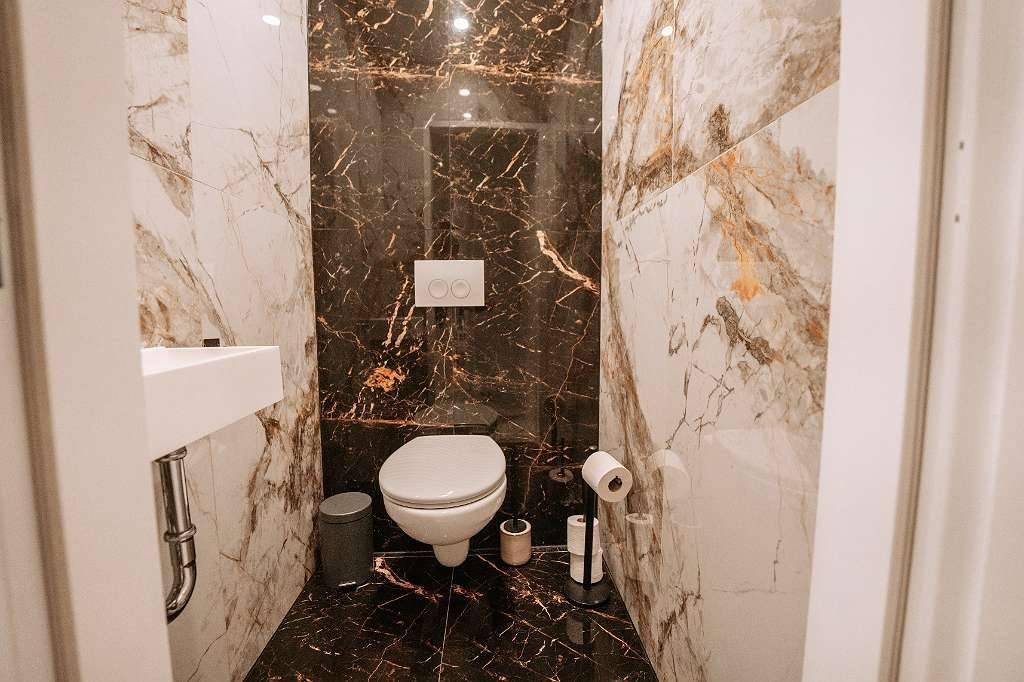 Kleines Gäste-WC mit modernen Marmorfliesen und wandmontierter Toilette.