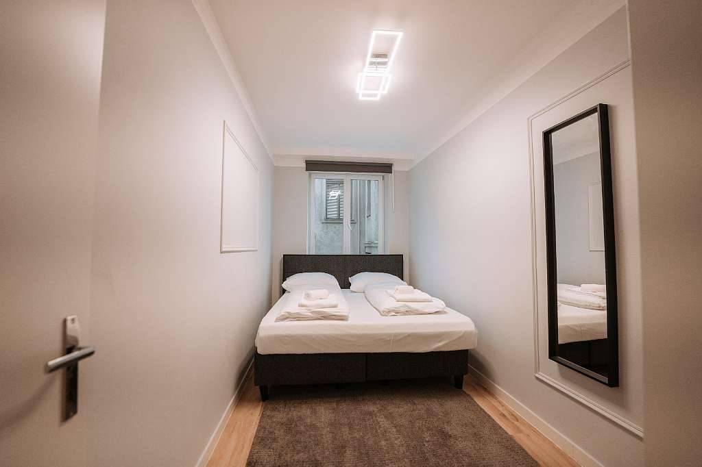 Kompaktes Schlafzimmer mit Doppelbett, Teppich und einem großen Spiegel.