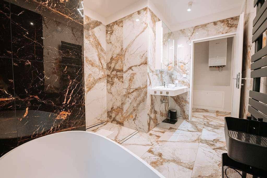 Geräumiges Badezimmer mit freistehender Badewanne, Duschbereich und luxuriösen Marmorfliesen.