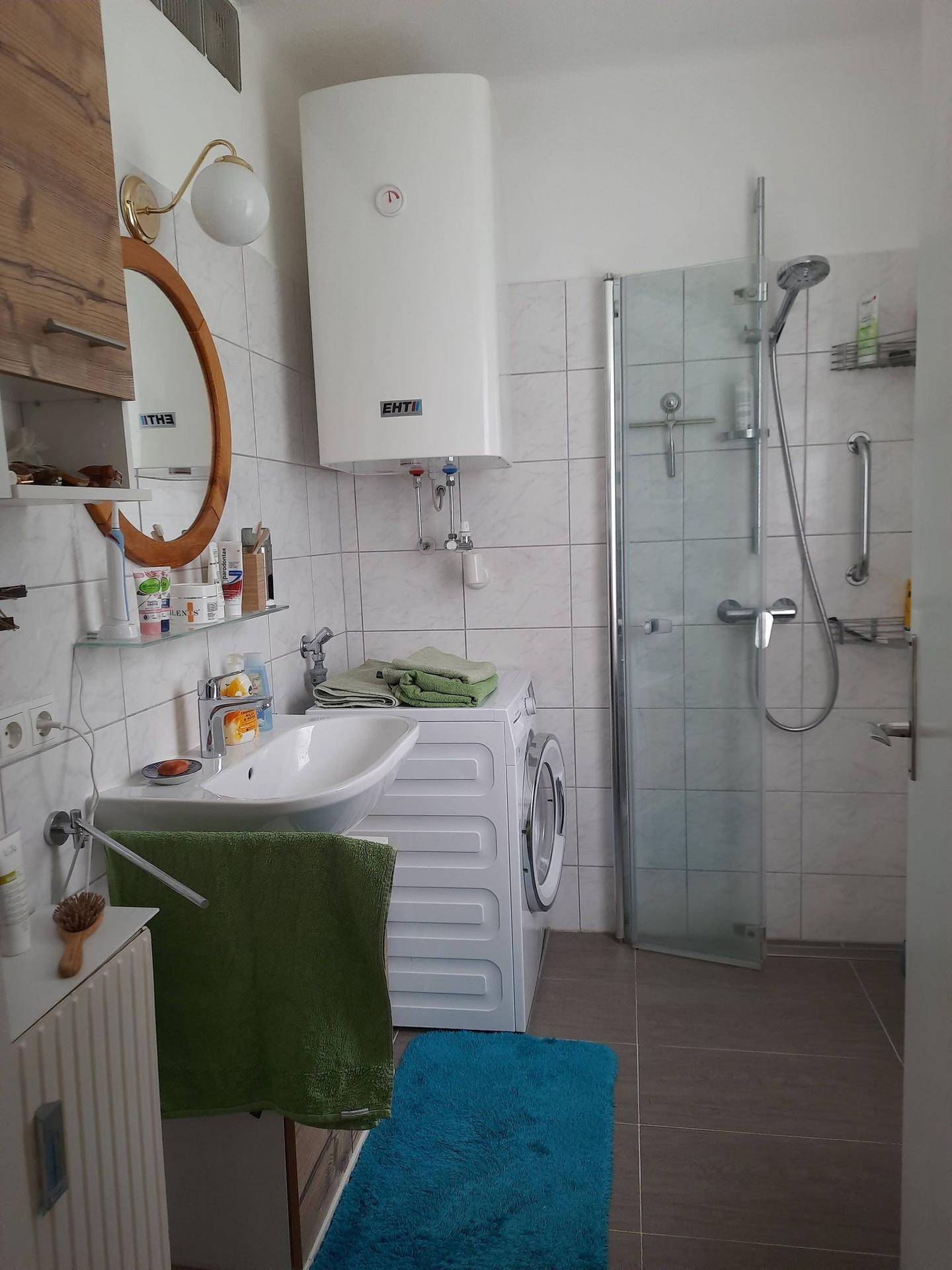 Badezimmer mit Dusche, Waschmaschine und hellen Wandfliesen in modernem Design.