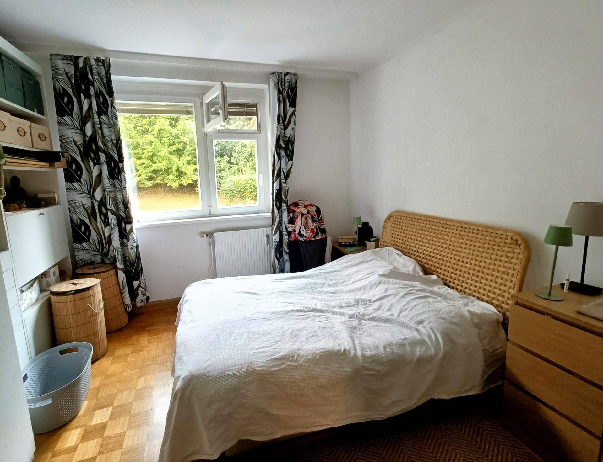 Schlafzimmer mit Doppelbett, Parkettboden und Fenster mit Blick ins Grüne.