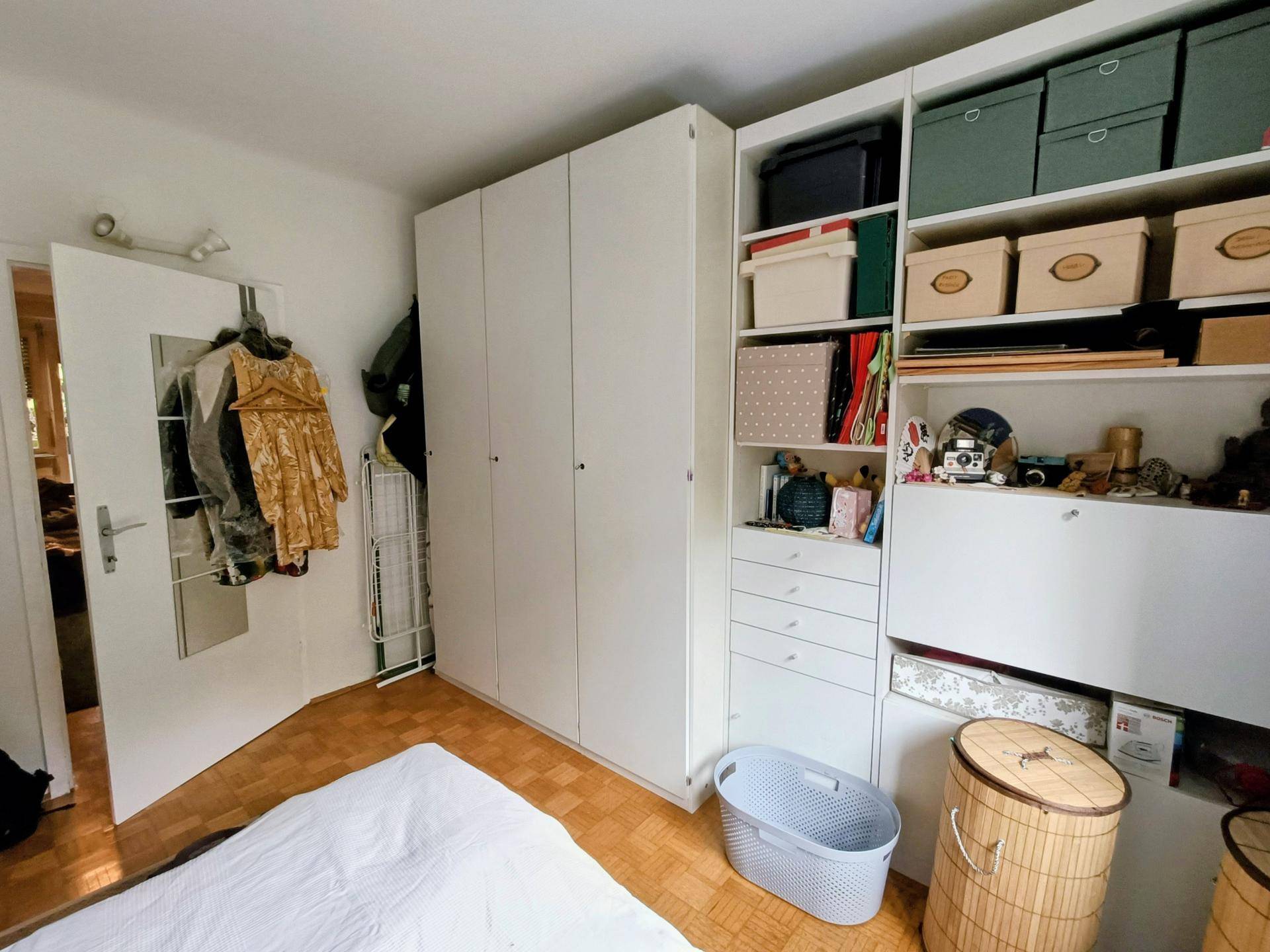 Schlafzimmer mit großem weißen Kleiderschrank und offenen Regalen für zusätzlichen Stauraum.