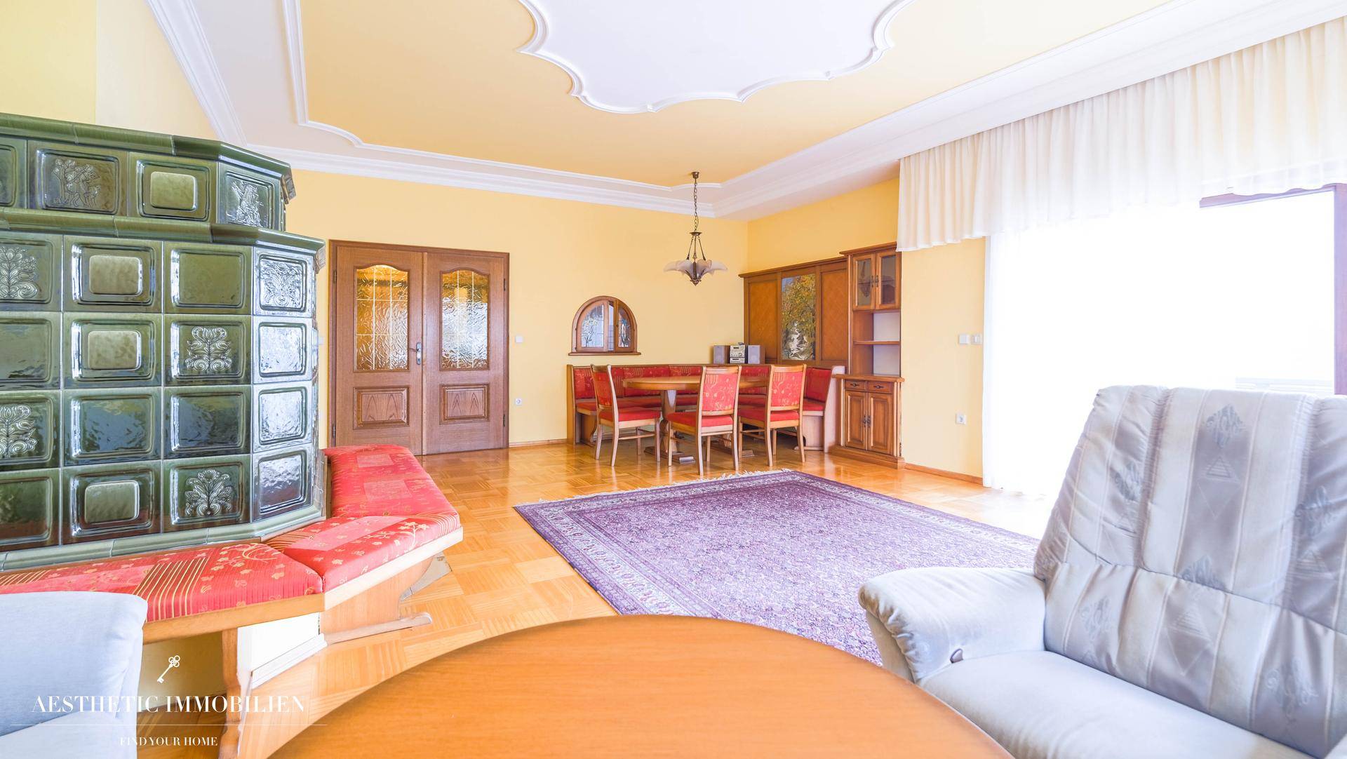 Traditioneller Essbereich mit Holztisch, Stühlen und Blick auf den Kachelofen.