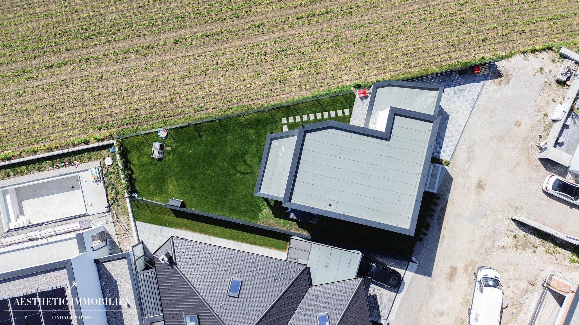 Luftaufnahme des modernen Hauses mit Flachdach, Garten und angrenzenden Feldern.