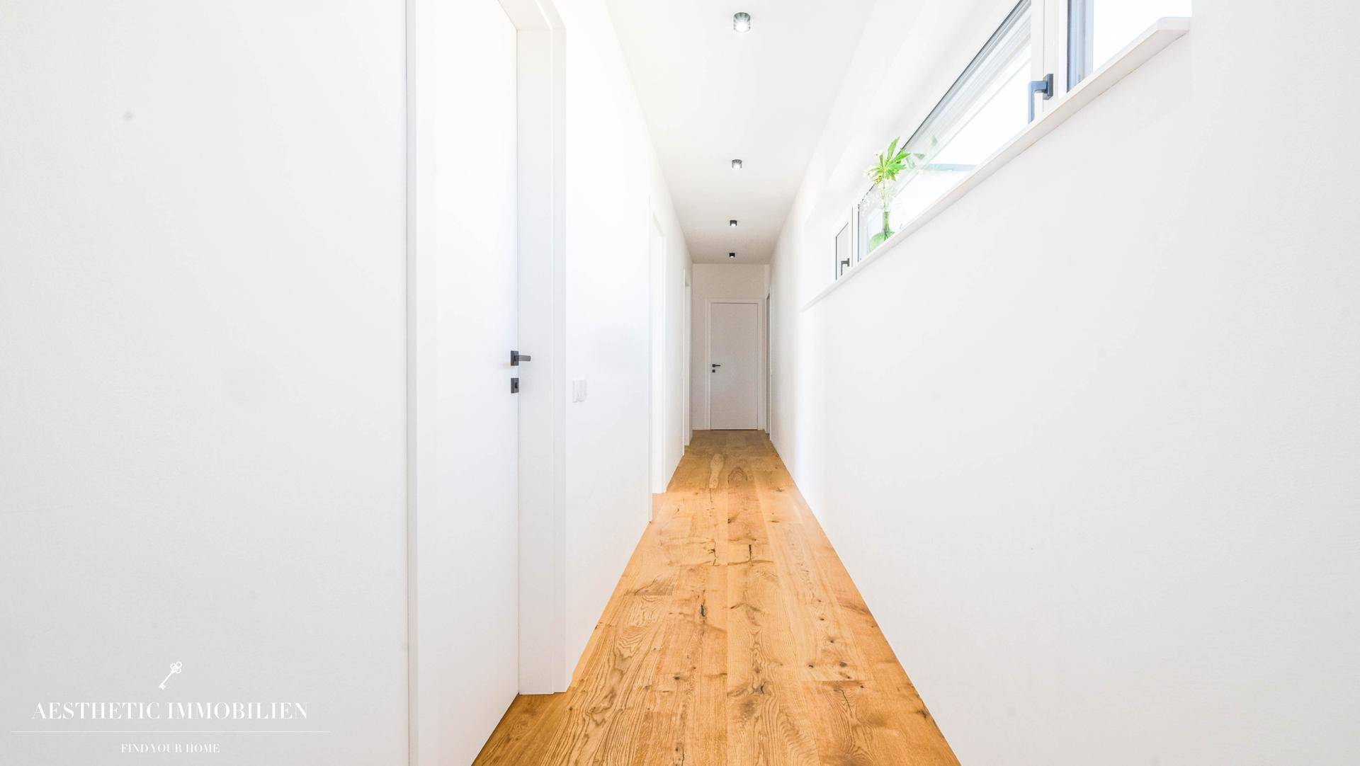 Langer, heller Flur mit Holzboden und schmalem Fenster für natürliches Licht.