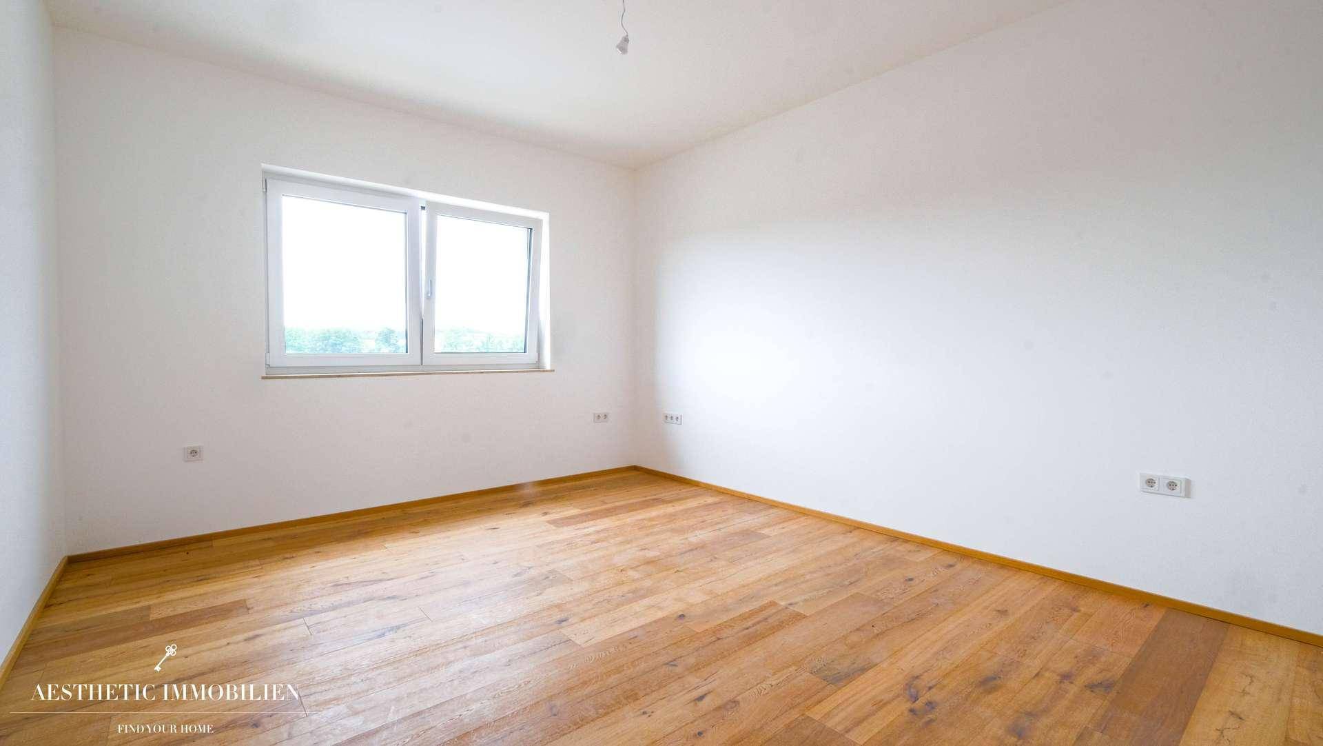 Helles, leeres Zimmer mit Holzboden und großem Fenster, ideal als Schlaf- oder Gästezimmer.