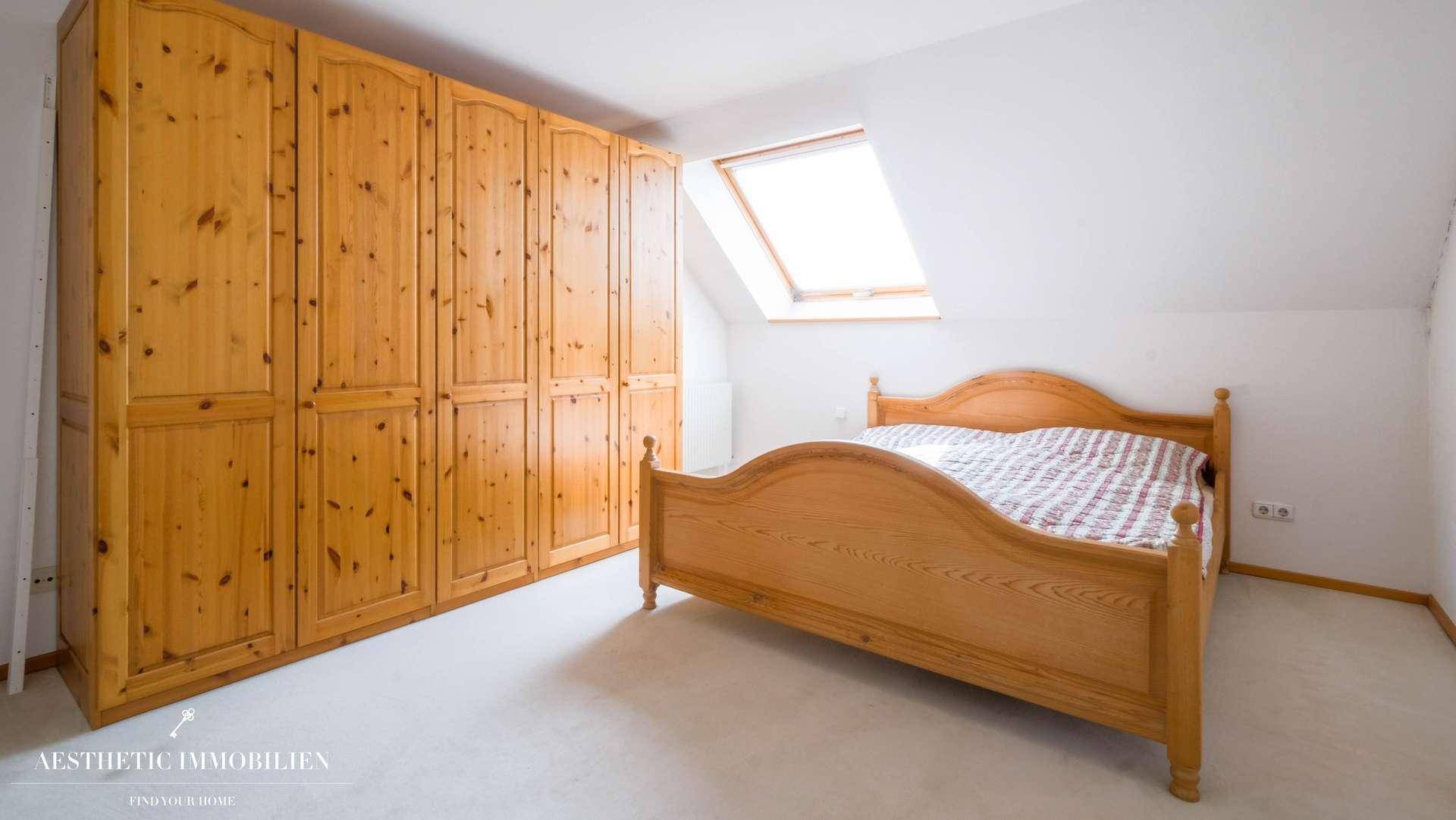Schlafzimmer im Dachgeschoss mit Holzbett, großem Kleiderschrank und Dachfenster.