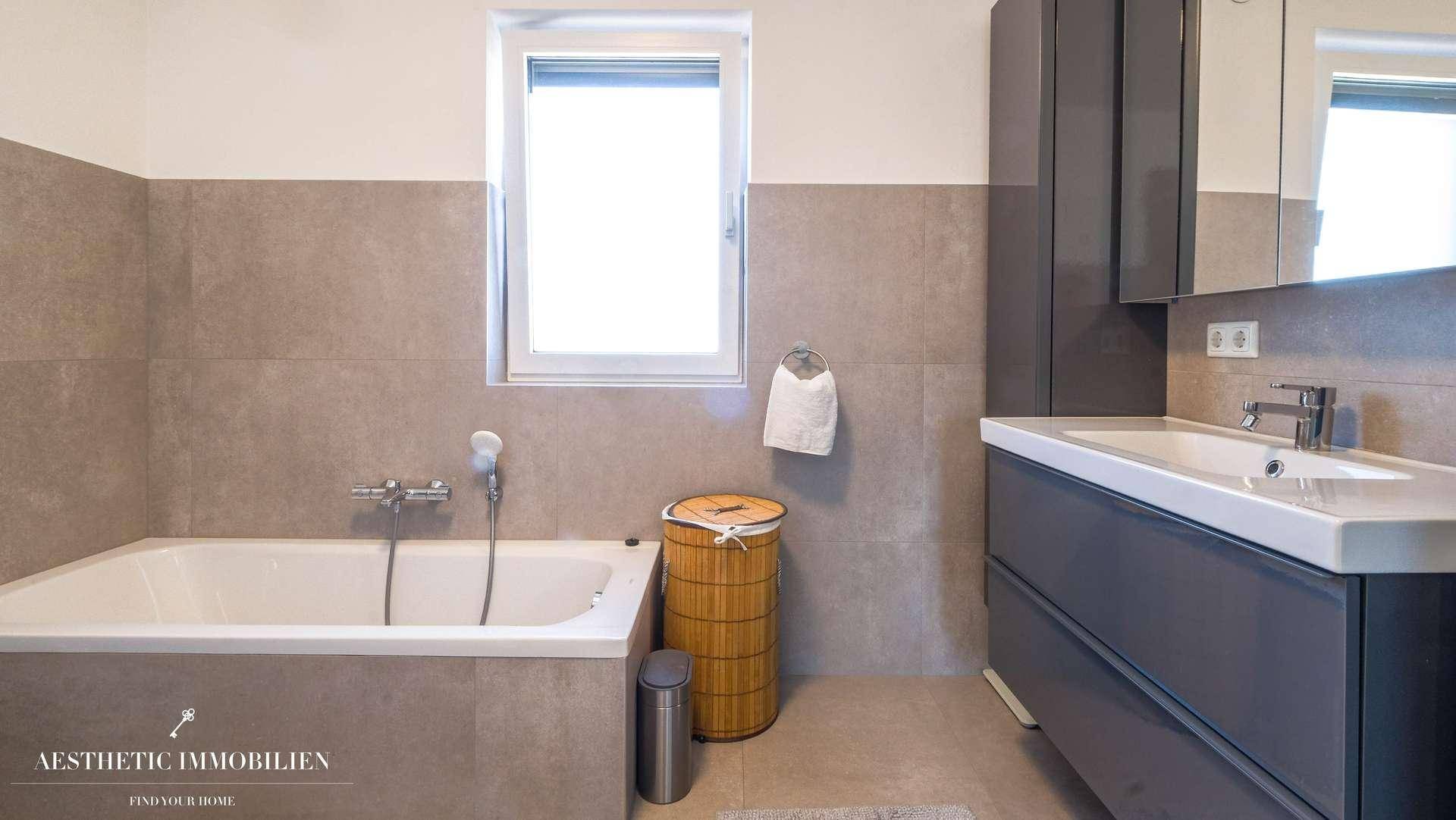 Helles Badezimmer mit Fenster, Badewanne, Waschtisch und Spiegelschrank.