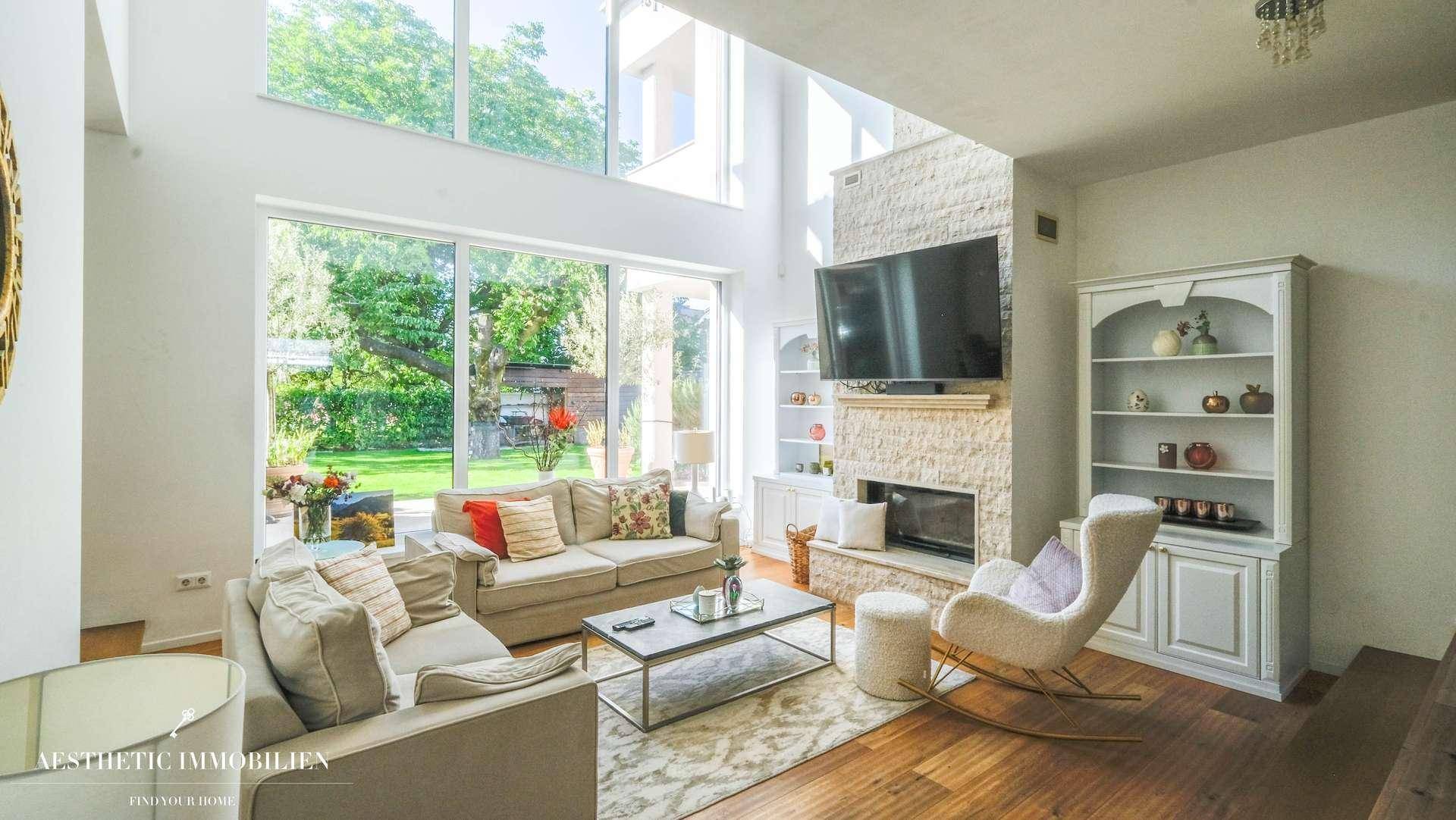 Helles Wohnzimmer mit hohen Decken, großen Fenstern und einem modernen Kamin.