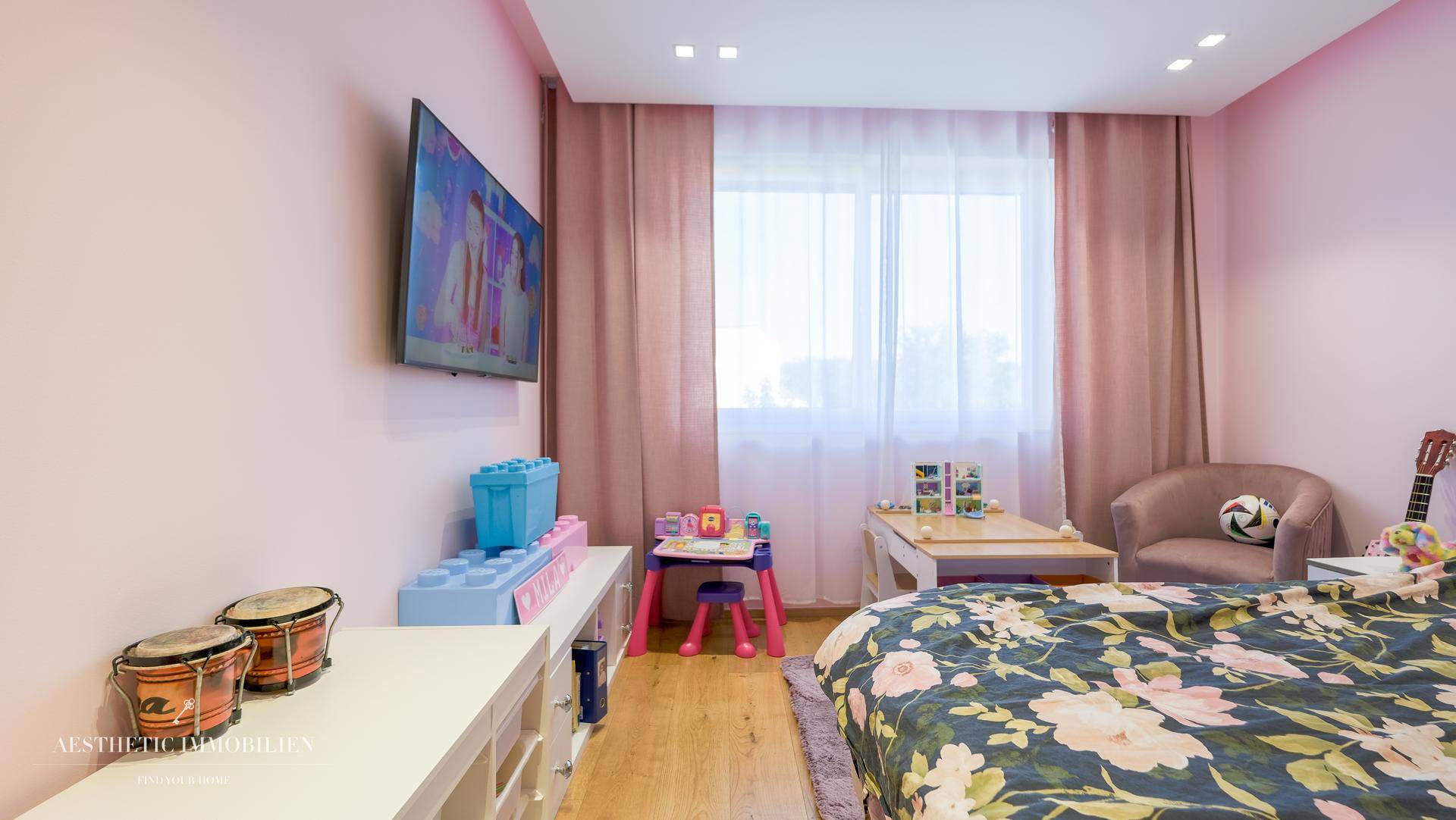 Helles Kinderzimmer mit Spielbereich, Holzboden und rosa Wandgestaltung.