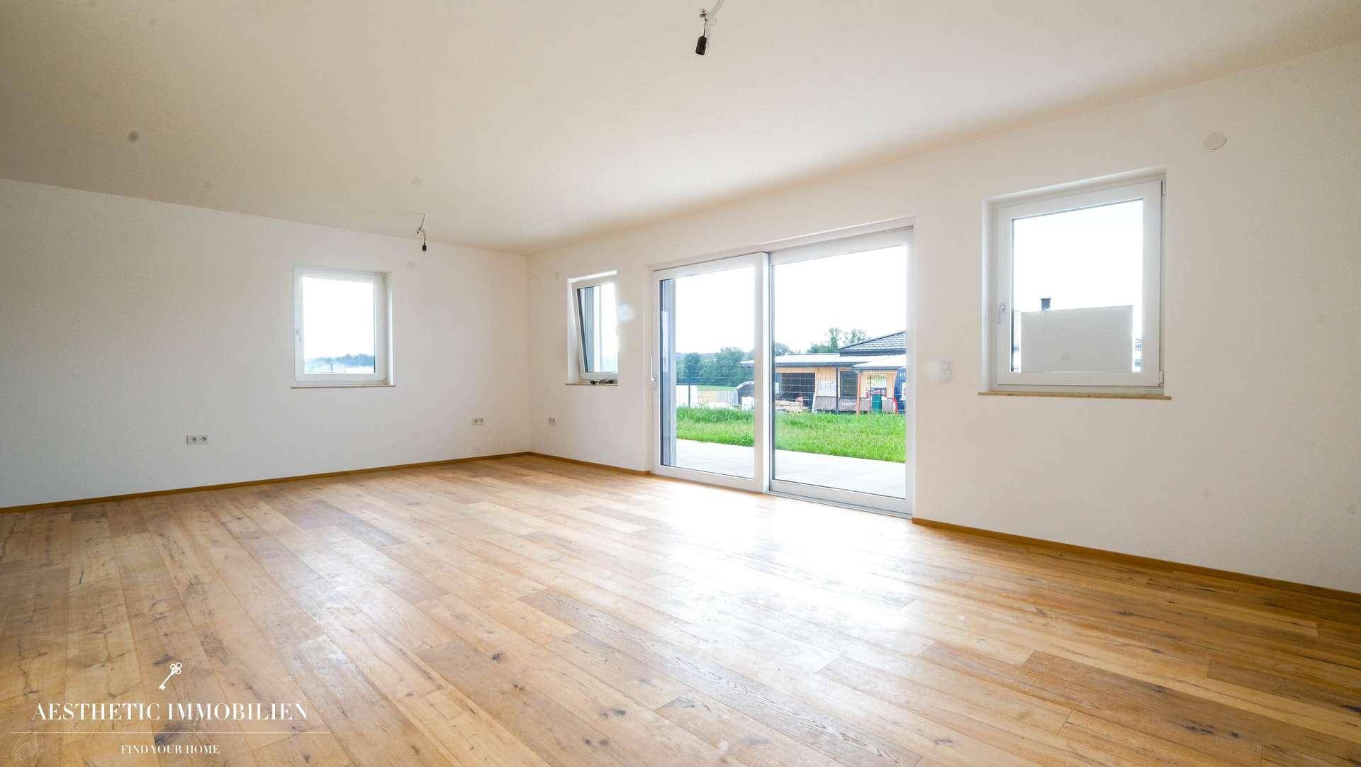 Geräumiges, leeres Wohnzimmer mit Holzboden und großen Schiebetüren zum Garten.