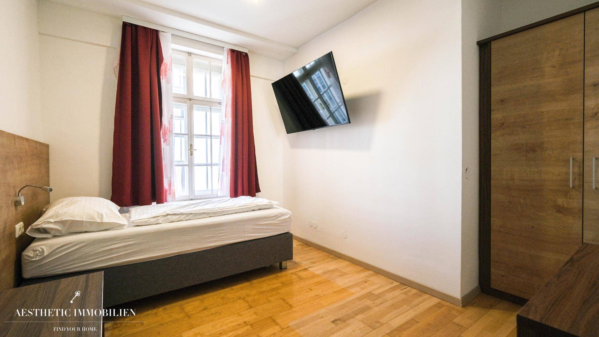 Helles Schlafzimmer mit Einzelbett, Holzboden und Wandfernseher.