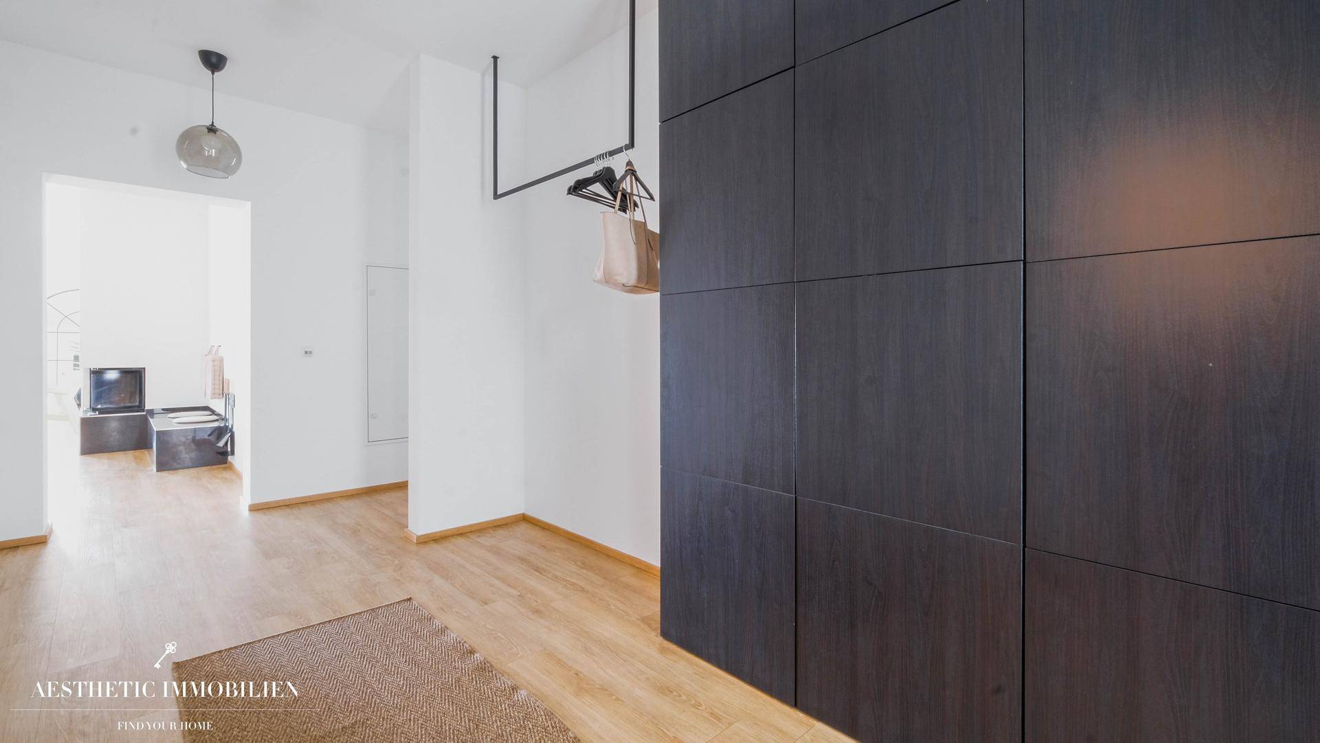 Heller Flur mit Holzboden und integrierten dunklen Schränken für Stauraum.