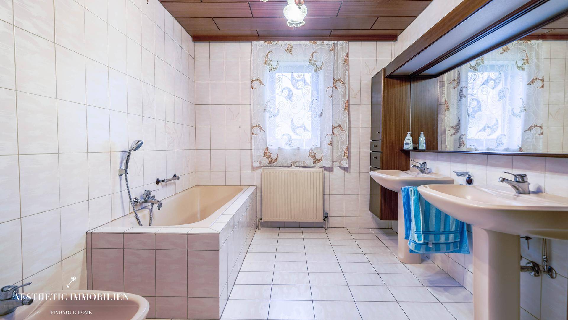 Badezimmer im 80er-Jahre-Stil mit Badewanne, Doppelwaschbecken und Holzdecke.