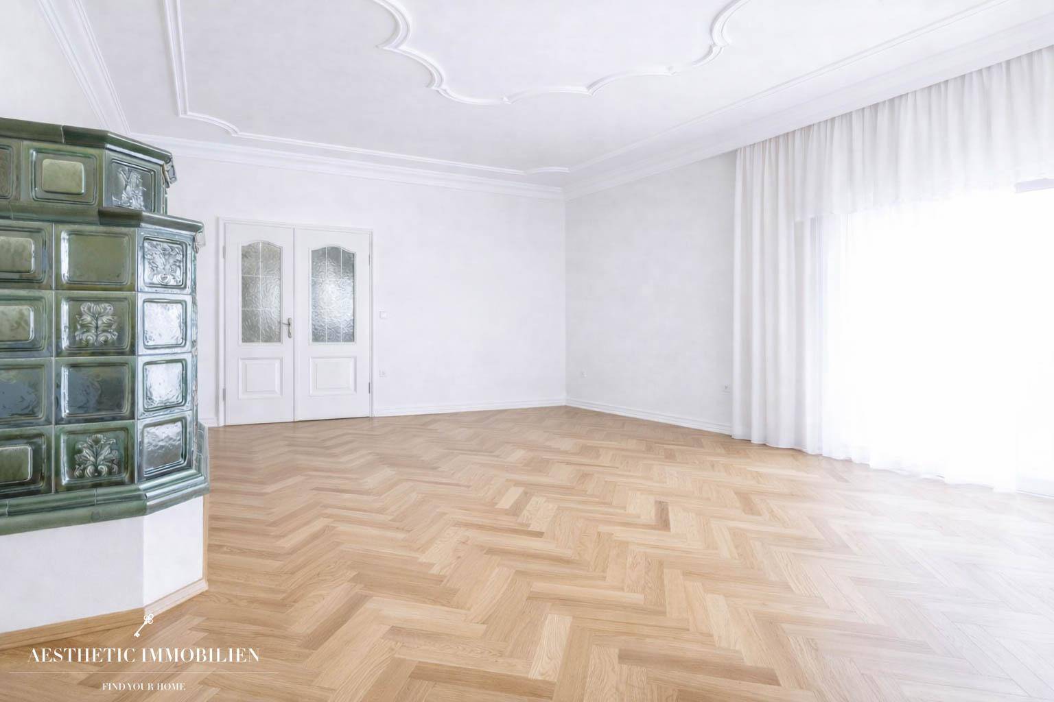 Helles, leeres Zimmer mit Fischgrätparkett, Stuckdecke und großem Fenster.