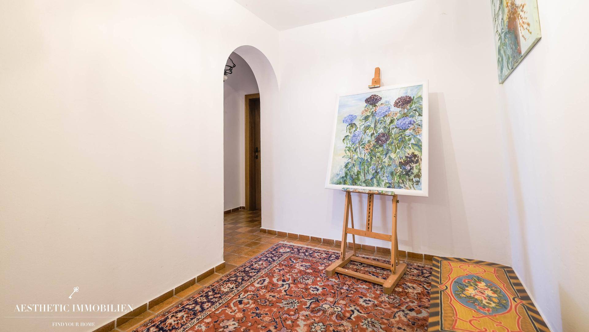 Heller Flur mit Fliesenboden, Teppich und Kunstwerken an den Wänden.