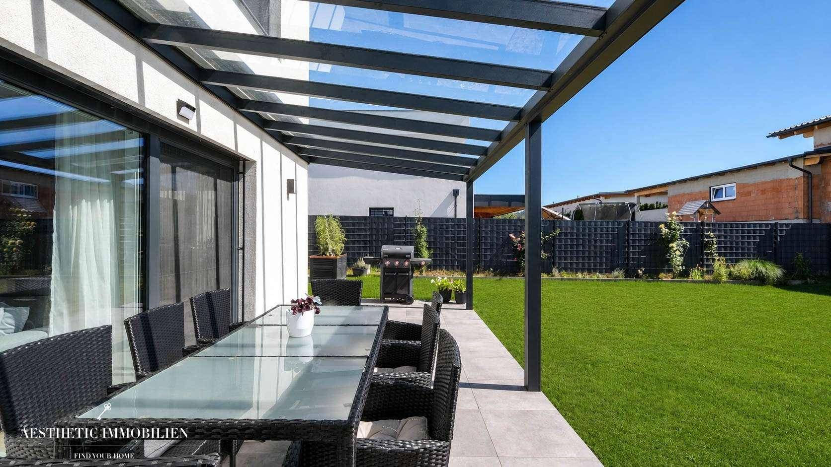 Überdachte Terrasse mit Gartenmöbeln und Blick auf den gepflegten Rasen.