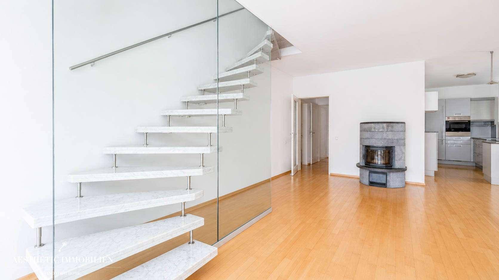 Elegante, moderne Treppe mit Glasgeländer und Holzstufen, angrenzend an Wohnbereich und Küche.