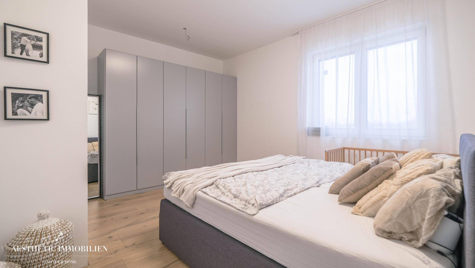 Helles Schlafzimmer mit Einbauschränken, Holzboden und großem Fenster.