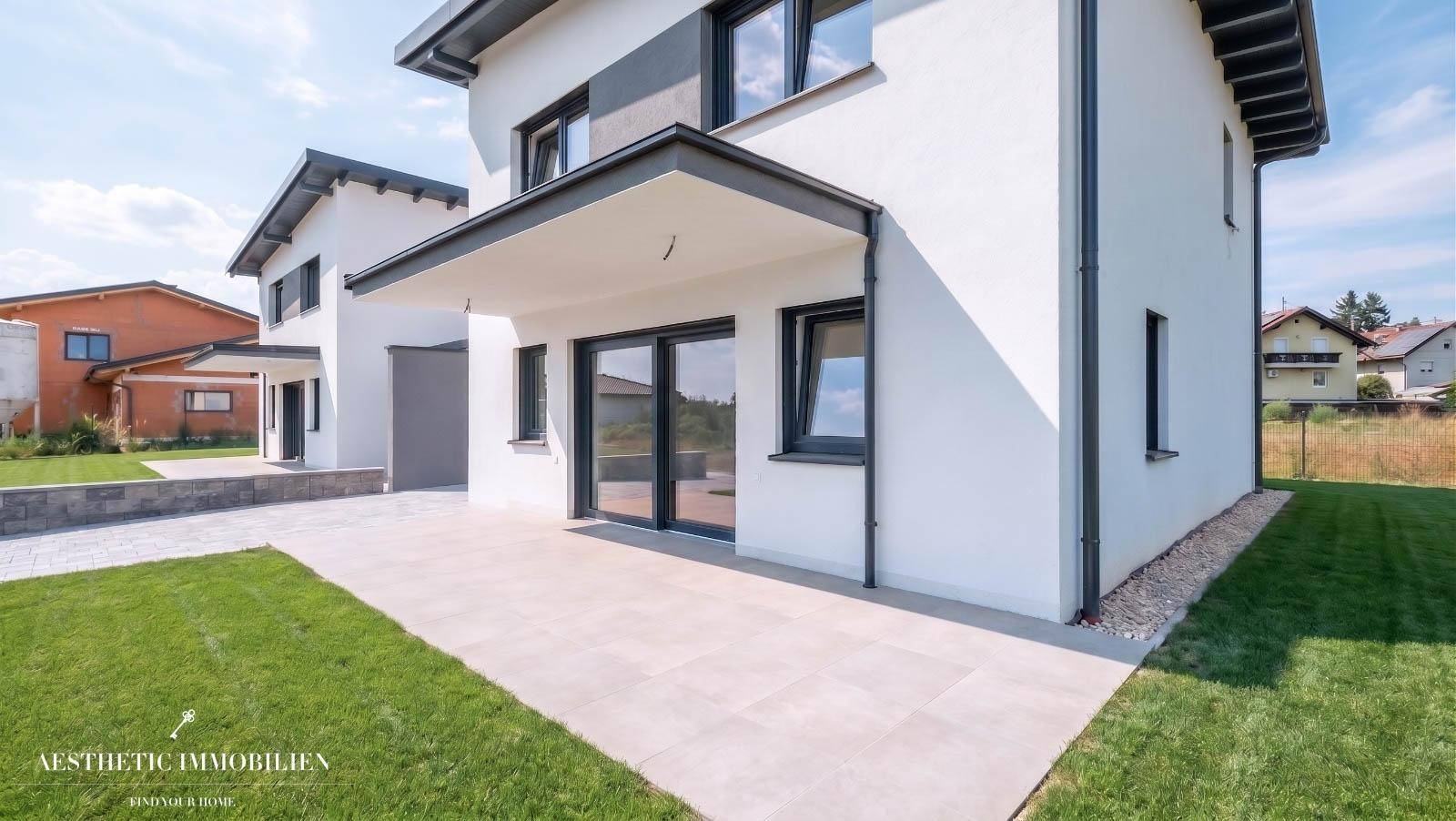 Hinterer Bereich des Hauses mit großer, gepflasterter Terrasse und angrenzender Rasenfläche.