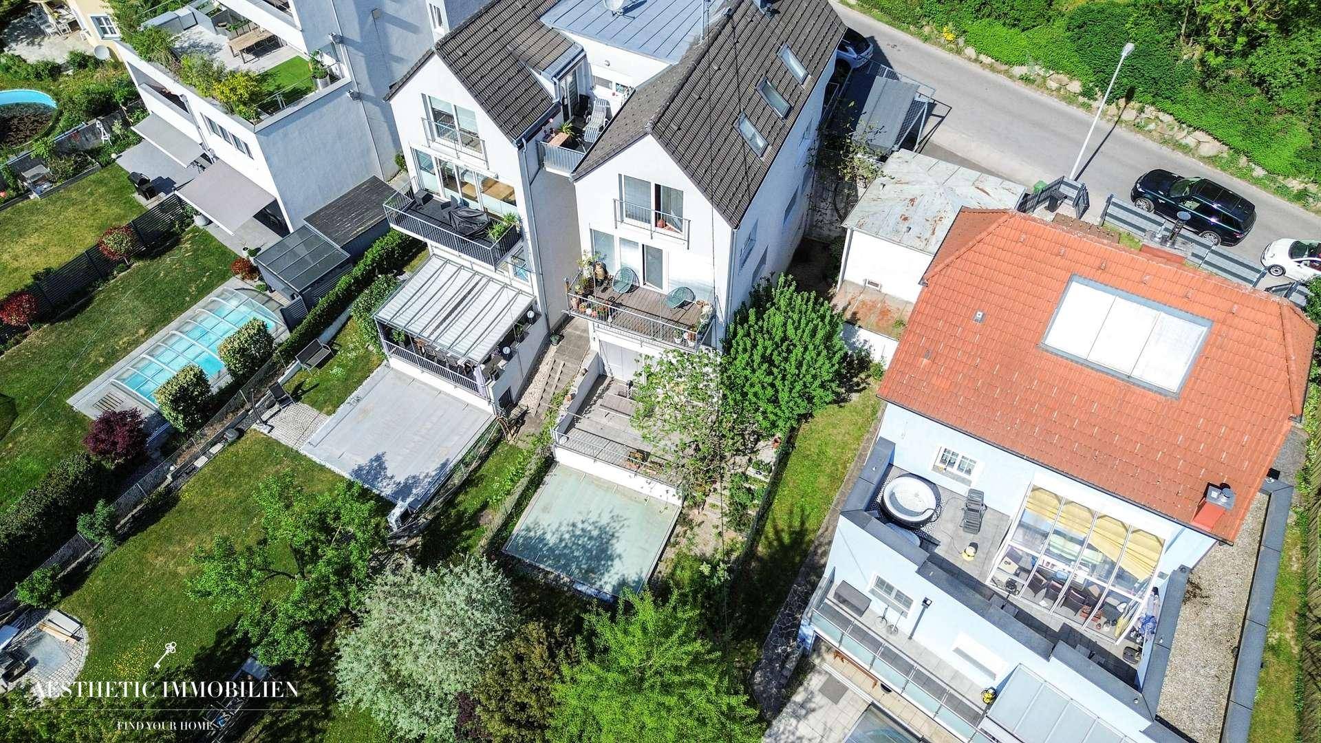 Luftaufnahme einer Wohnsiedlung mit mehreren Häusern, Gärten und angrenzender Straße.