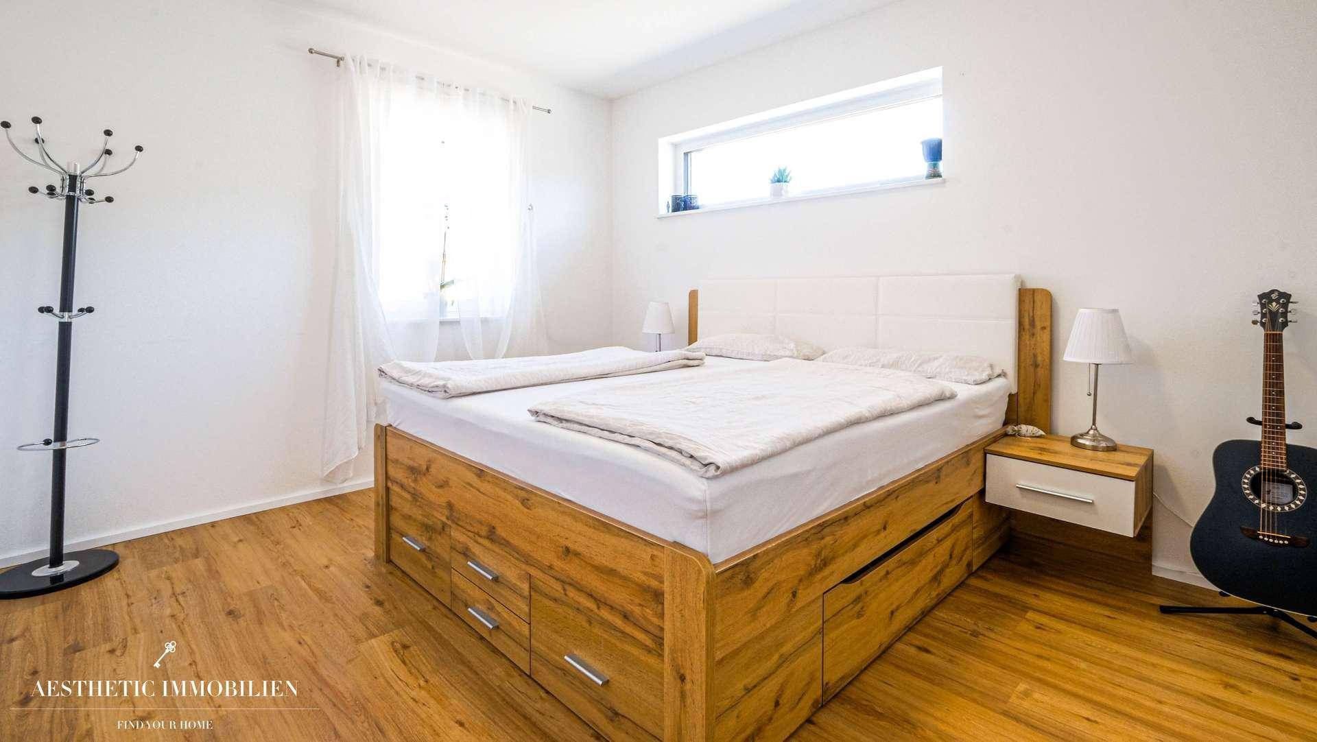 Schlafzimmer mit Holzbett, Stauraum und großem Fenster für viel Tageslicht.
