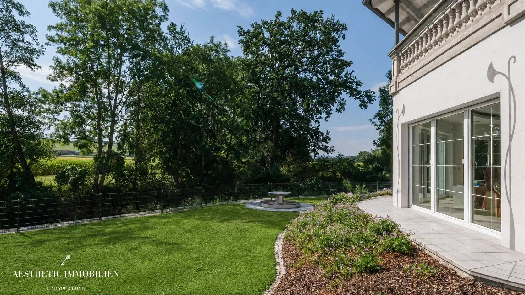 Gepflegter Gartenbereich mit Rasenfläche, Sträuchern und einem kleinen Brunnen.