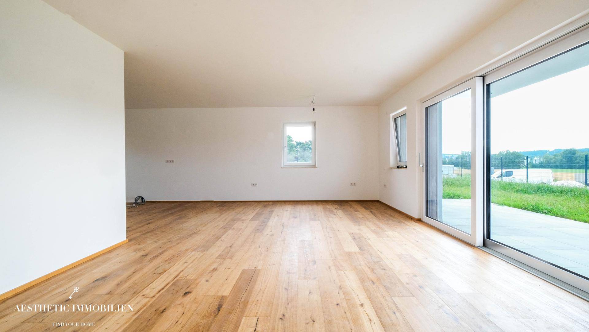 Lichtdurchfluteter, leerer Raum mit Holzboden und breiter Schiebetür zum Garten oder zur Terrasse.