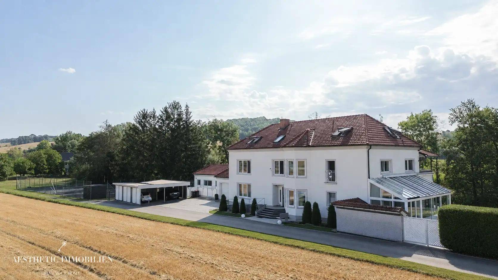 Weitläufiges Anwesen mit Haupthaus, Carport und umliegenden Feldern in ländlicher Umgebung.