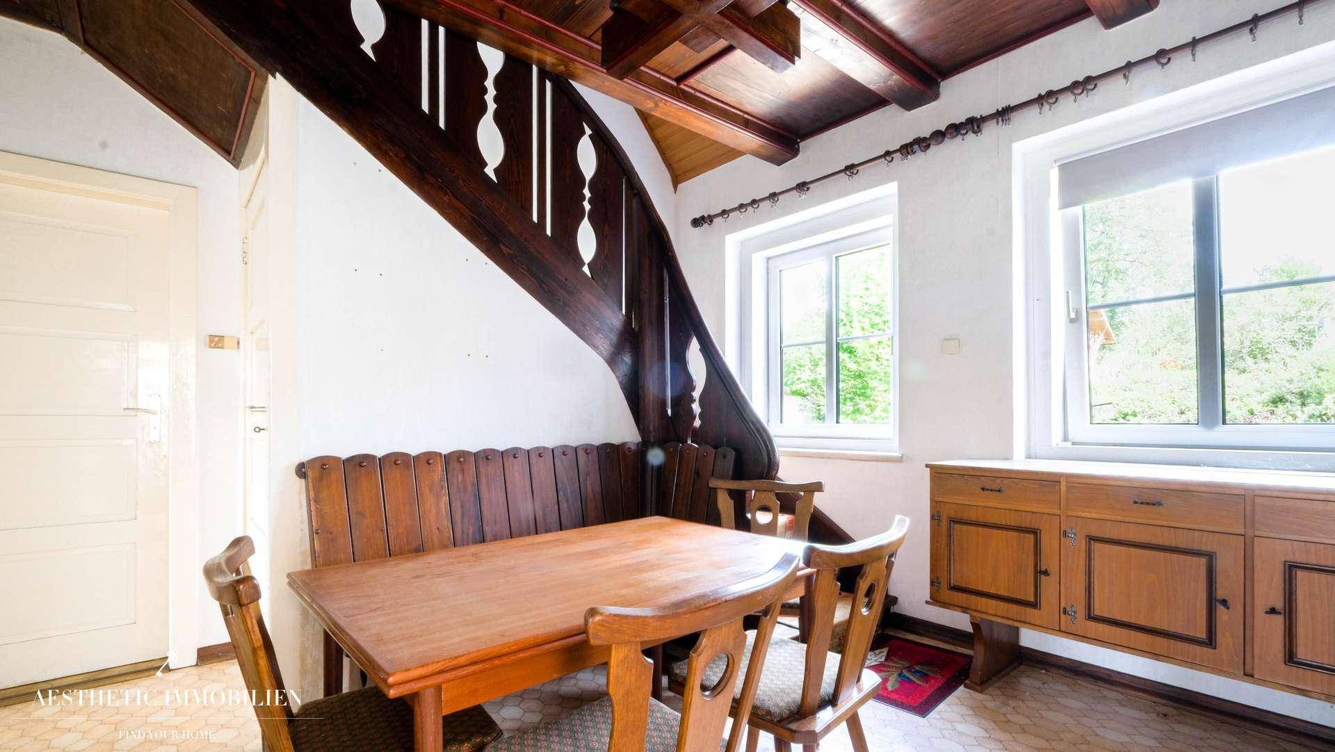 Traditioneller Essbereich mit rustikalen Holzmöbeln und sichtbarer Holztreppe.