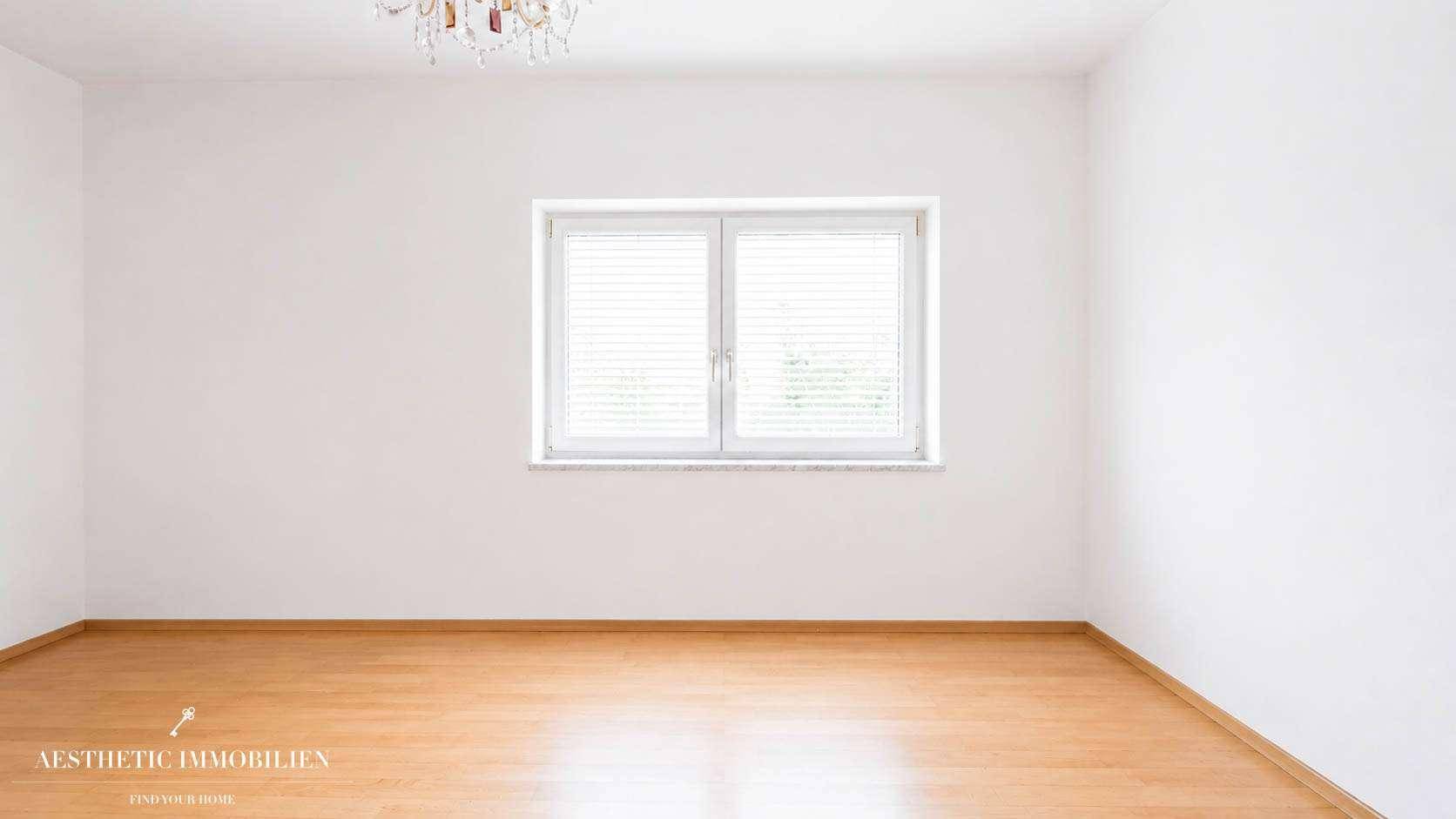 Leeres Zimmer mit hellem Holzboden, weißen Wänden und einem Fenster, bereit zur individuellen Gestaltung.