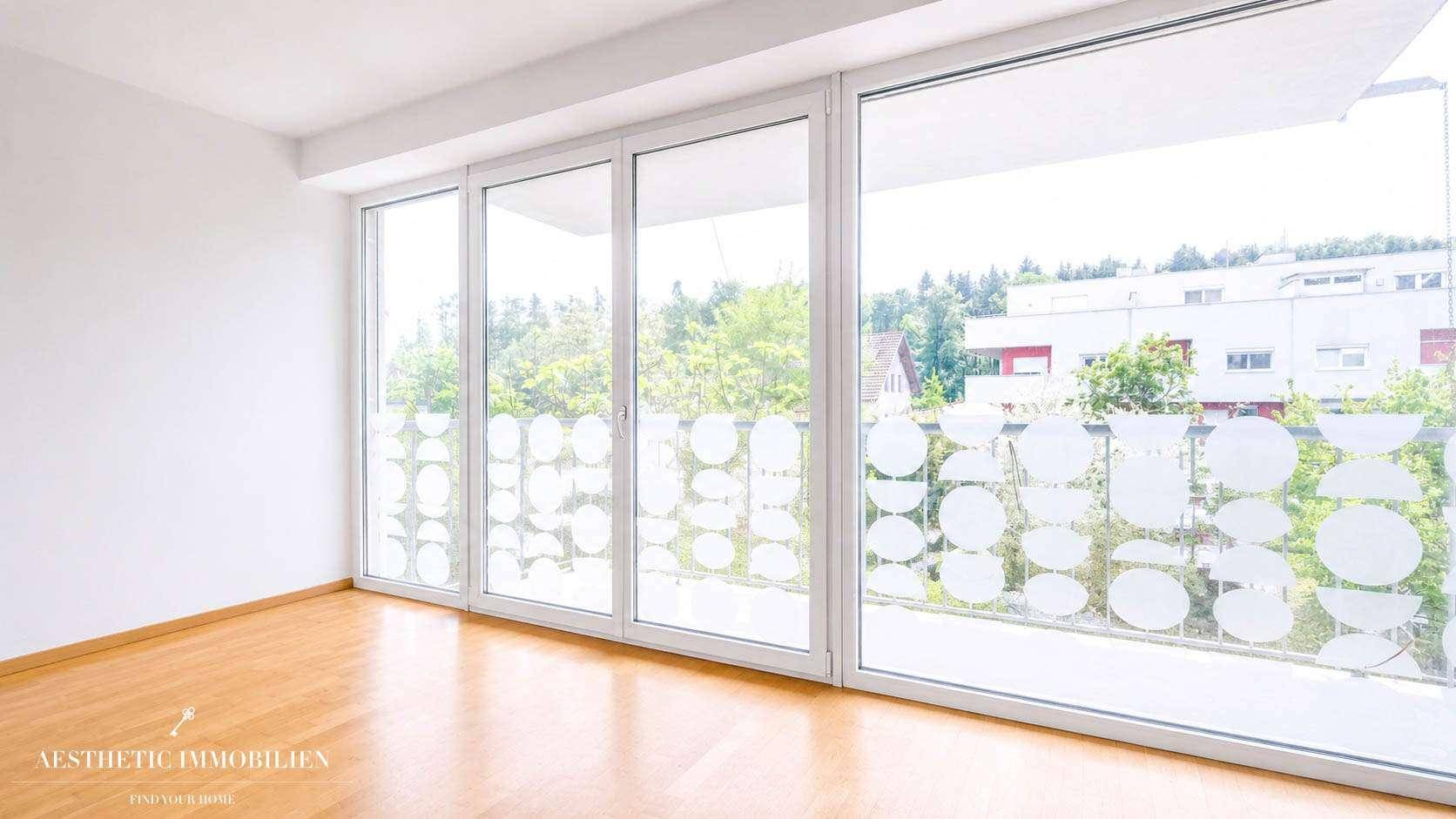 Leeres Schlafzimmer mit großen Fenstern, die einen weiten Blick ins Grüne ermöglichen.