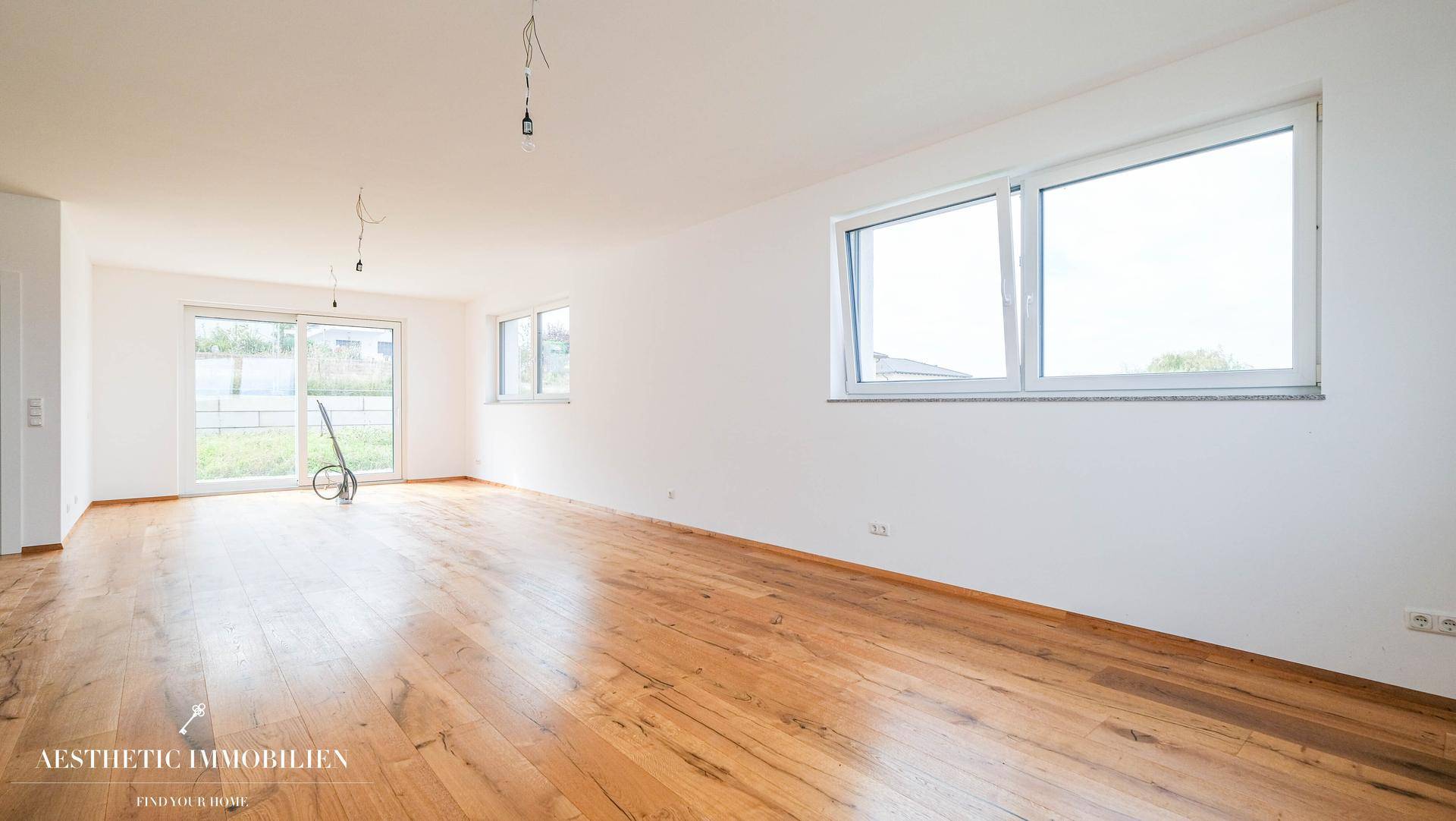 Heller, unmöblierter Raum mit Holzboden und großen Fenstern, ideal für einen Wohnbereich.