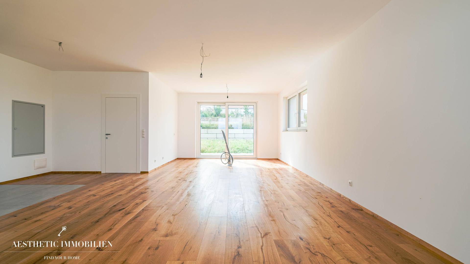 Geräumiger, unmöblierter Wohnbereich mit hellem Holzboden und großen Fenstern für viel Tageslicht.